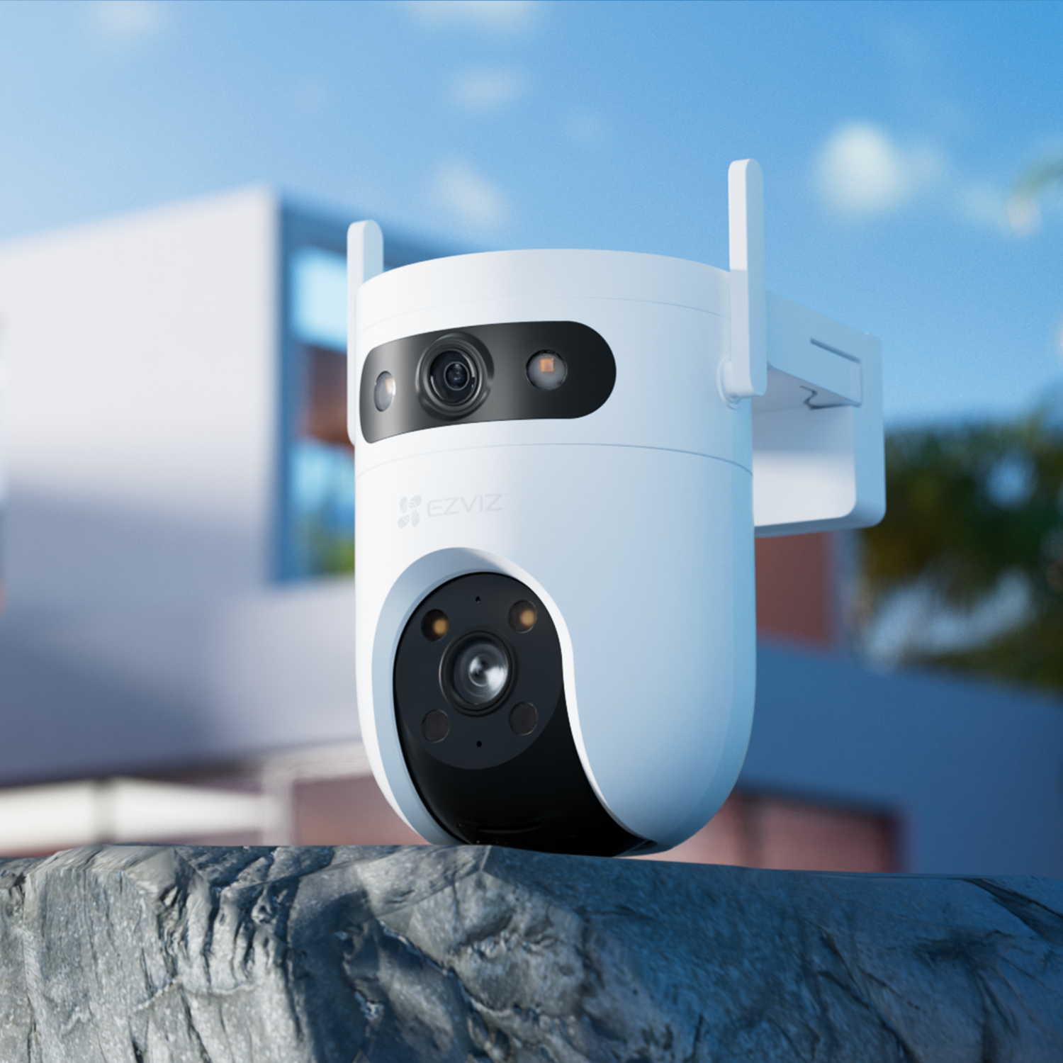 A white security camera with antennas is mounted on a rock. A building and blue sky are visible in the background.