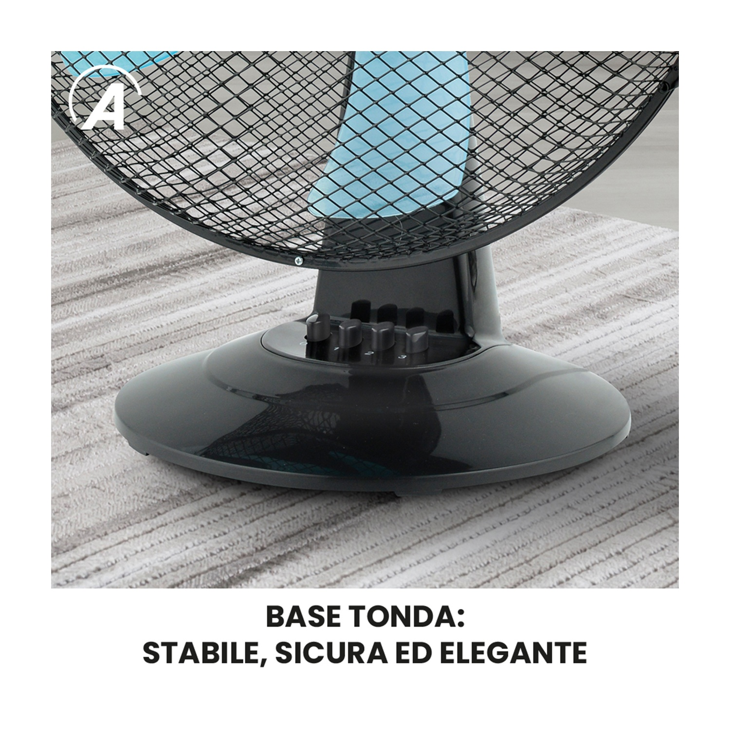 Un ventilatore nero con griglia protettiva su un tappeto. La base è rotonda e nera. Un elemento blu è visibile dietro la griglia.