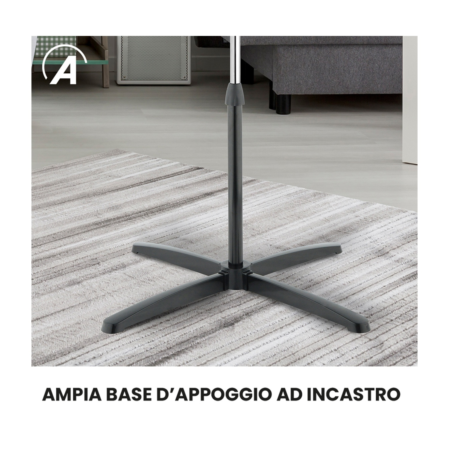 Una base nera del ventilatore con quattro gambe su un tappeto fantasia. Un palo di metallo si estende verso l'alto. Un divano sullo sfondo.