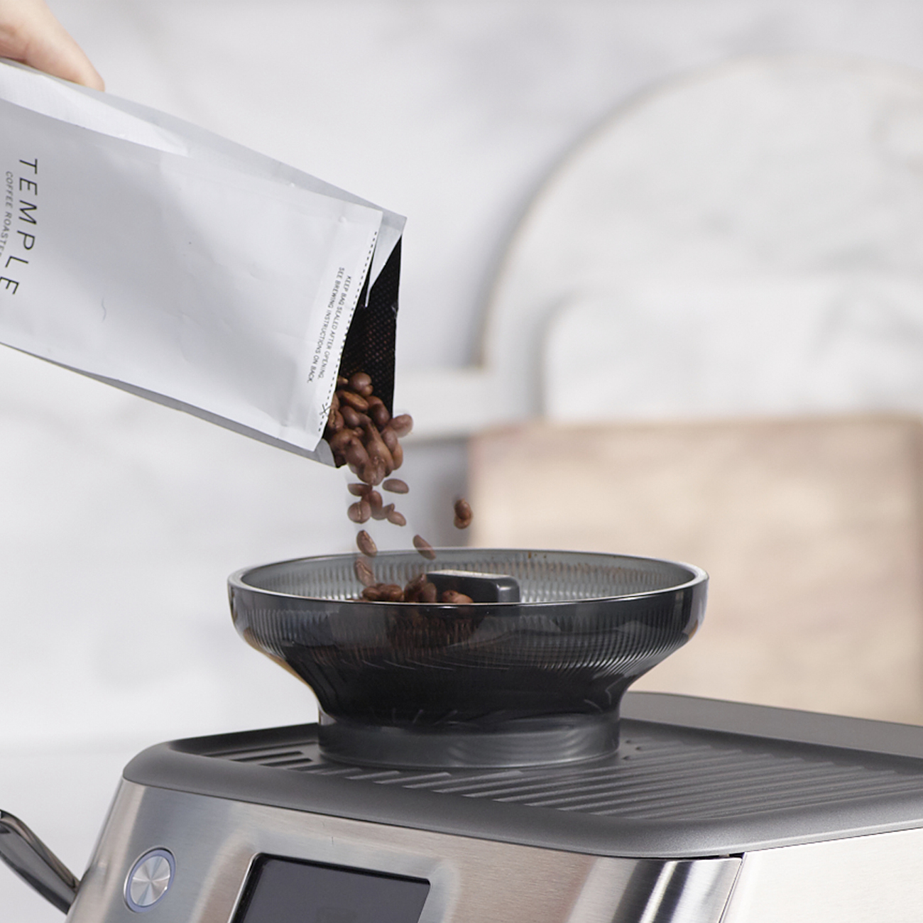 I chicchi di caffè vengono versati da un sacchetto Temple Roastery in una ciotola nera su una macchina da caffè argentata.