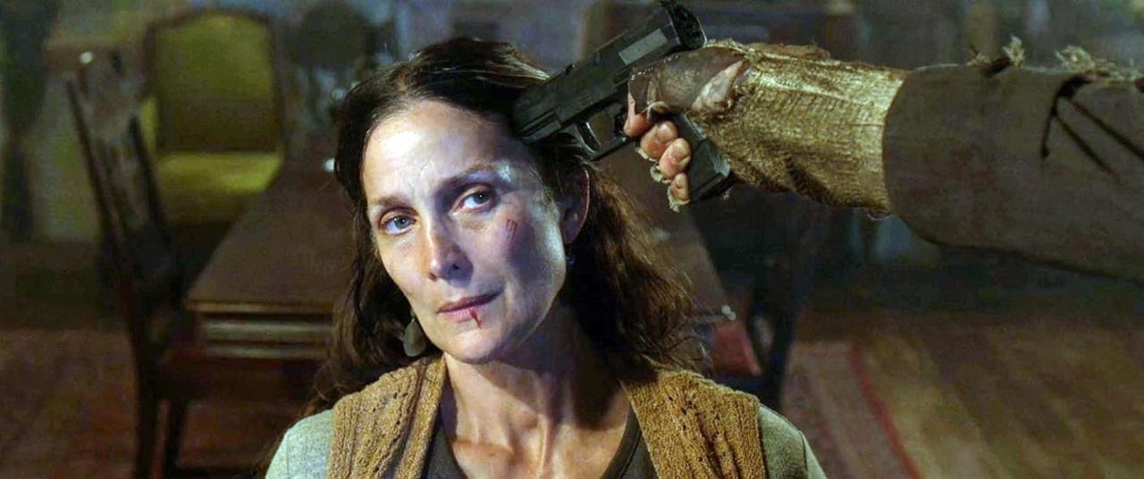 Das Gesicht einer Frau mit einer Waffe, die auf ihren Kopf gerichtet ist. Eine Hand hält die Waffe. Die Frau hat eine Schnittwunde im Gesicht und Blut auf der Lippe.