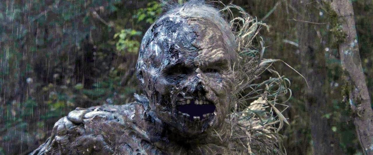 Eine zombieartige Gestalt mit verfallender Haut und offenem Mund steht in einem regnerischen Wald. Grünes Laub umgibt die Kreatur.