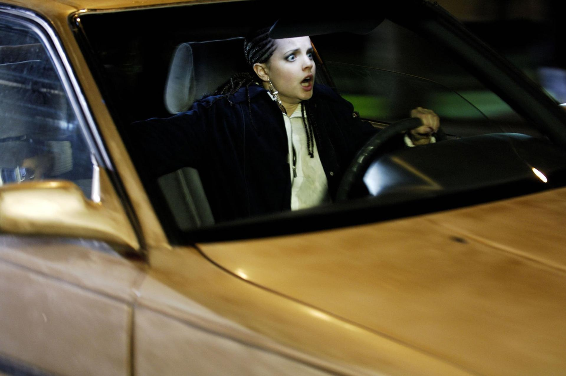 Eine Frau im Auto schaut geschockt, die Augen weit aufgerissen. Sie fährt nachts. Das Auto ist beige.