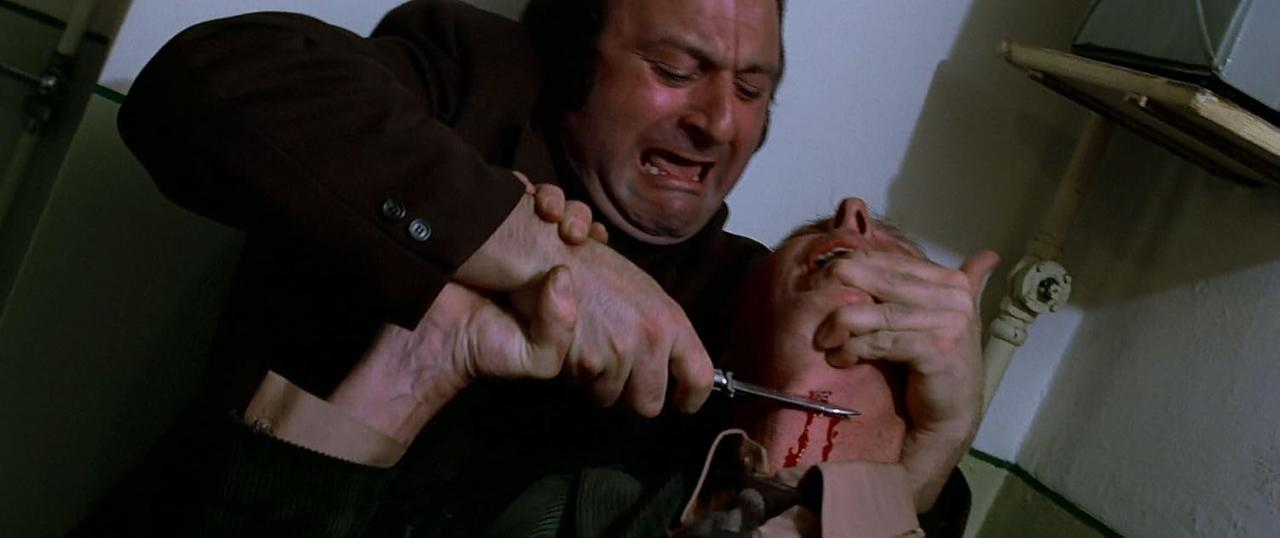 Ein Mann greift einen anderen mit einem Messer an. Blut ist sichtbar. Der Angreifer hält das Gesicht und den Hals des Opfers.