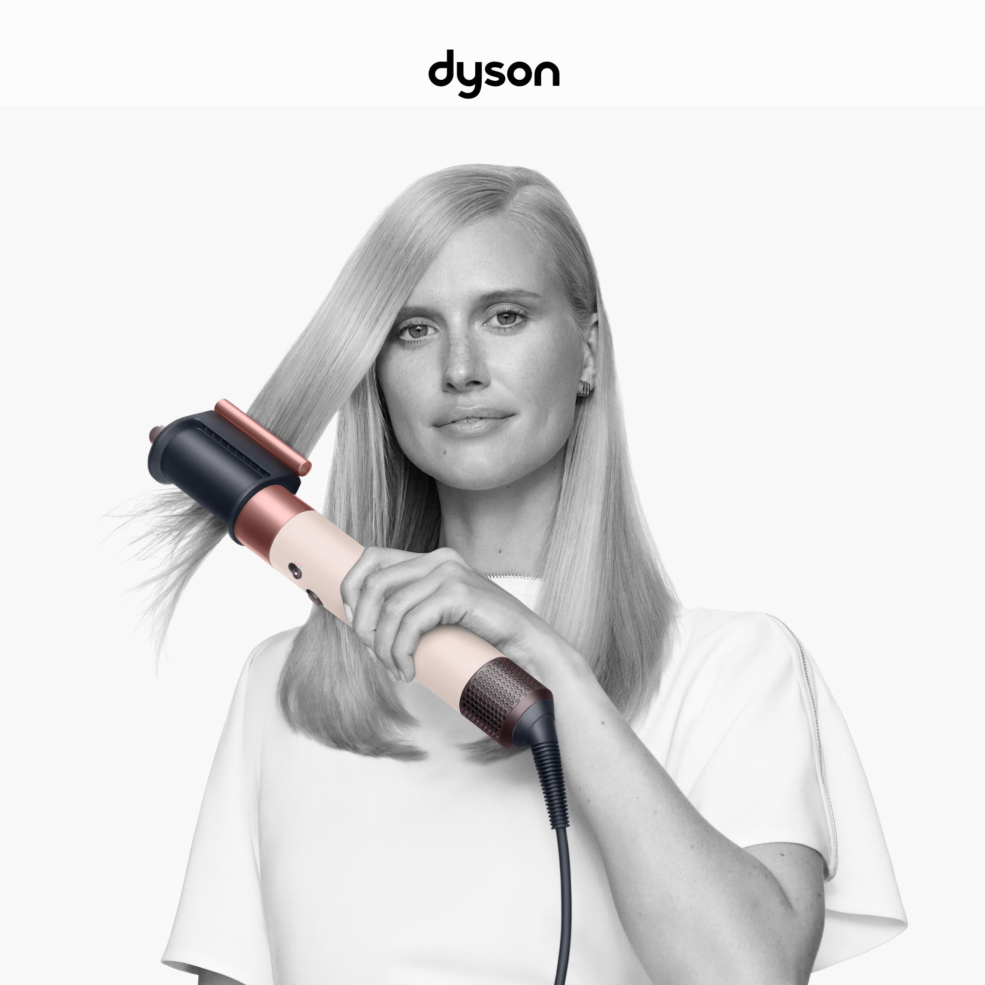 Blonde Frau benutzt einen Dyson-Haarstyler. Sie trägt ein weißes Oberteil. Der Hintergrund ist weiß, Dyson-Logo oben.