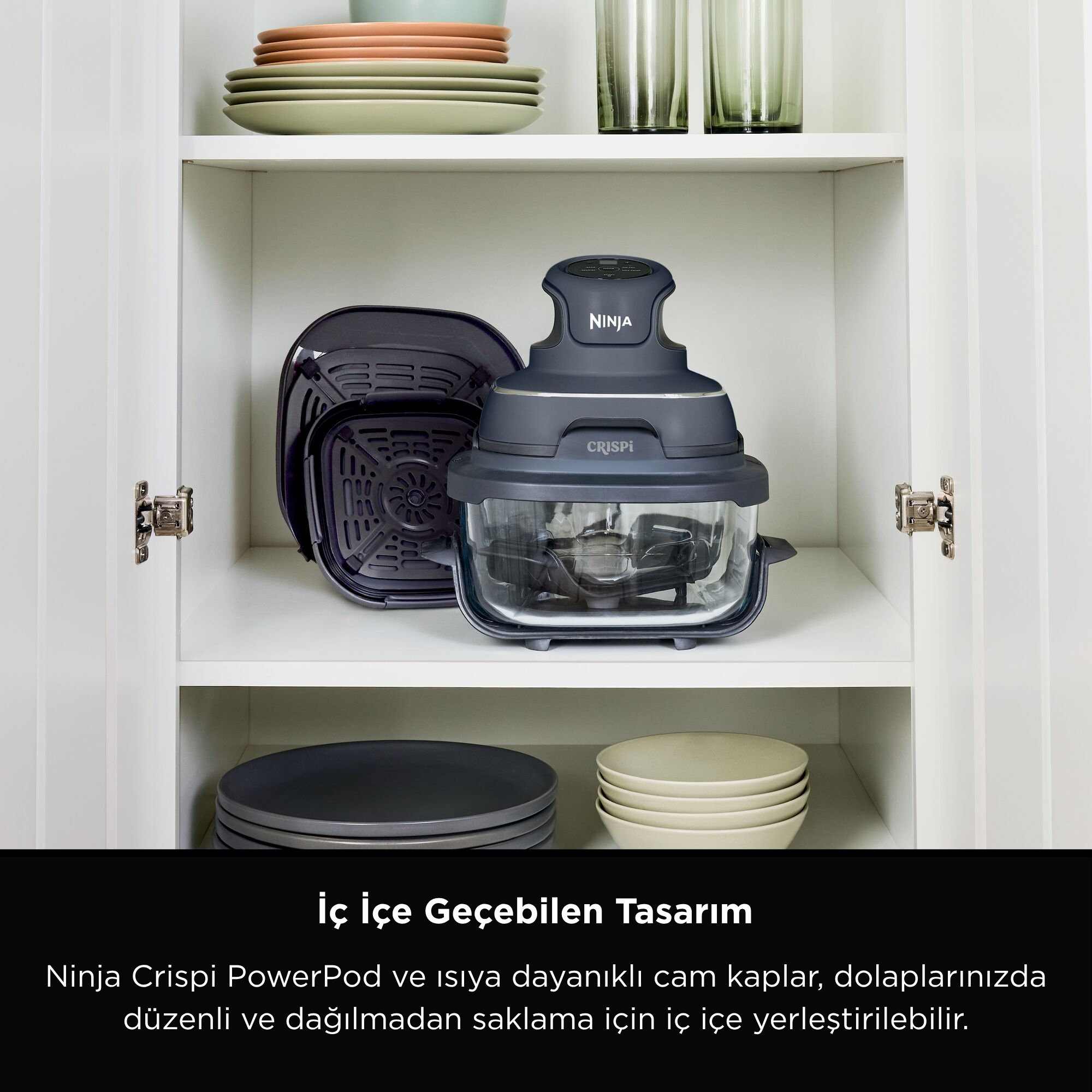 Beyaz bir dolapta Ninja Crispi PowerPod, tabaklar ve bardaklar var. Gri ve siyah renkte, cam bir kaseye sahip.