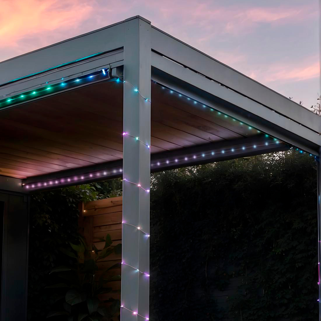 Pergola mit bunten Lichtern. Der Himmel ist rosa. Grüne, blaue und lila Lichter an den Rändern und Stützen der Pergola.