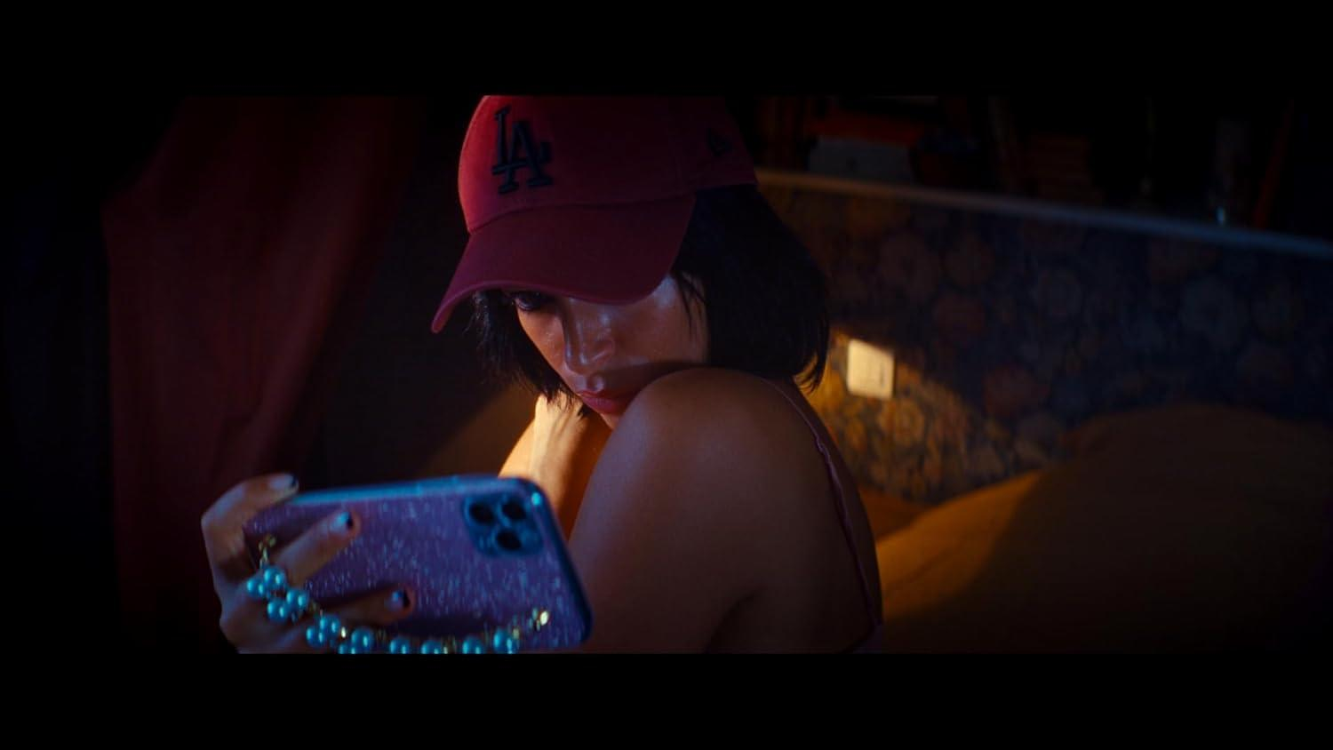 Eine Frau mit roter Kappe schaut auf ihr Handy. Sie hält das Telefon mit Perlenaccessoires. Der Hintergrund ist ein Bett.
