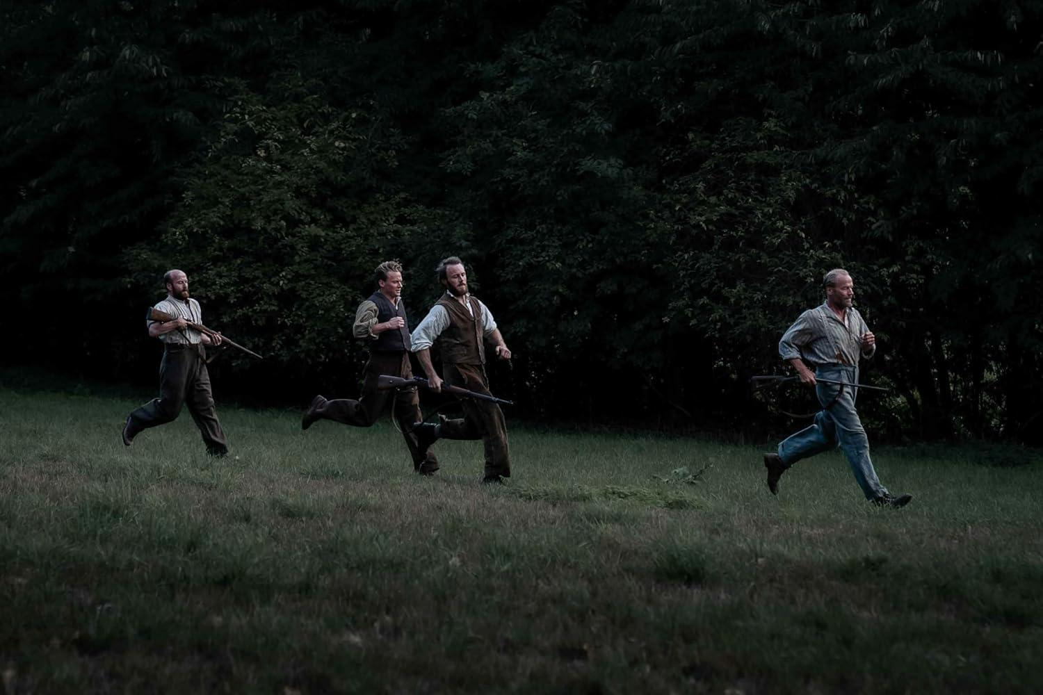 Vier Männer rennen über eine Wiese, jeder trägt ein Gewehr. Dunkle Bäume bilden den Hintergrund. Die Männer tragen historische Kleidung.