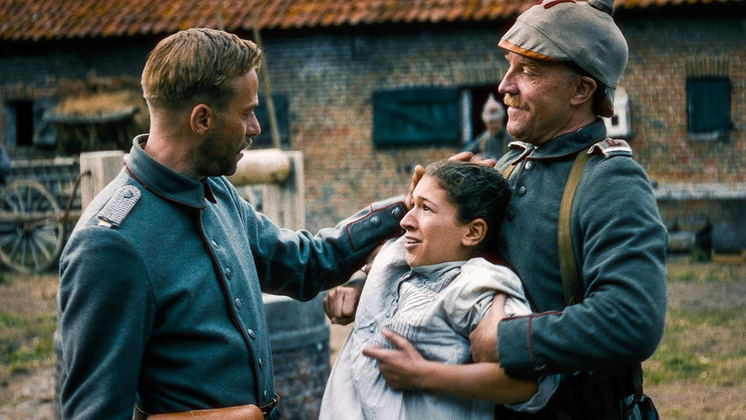 Zwei Soldaten halten eine verstörte Frau. Sie tragen graue Uniformen. Im Hintergrund ein Backsteingebäude mit rotem Dach.