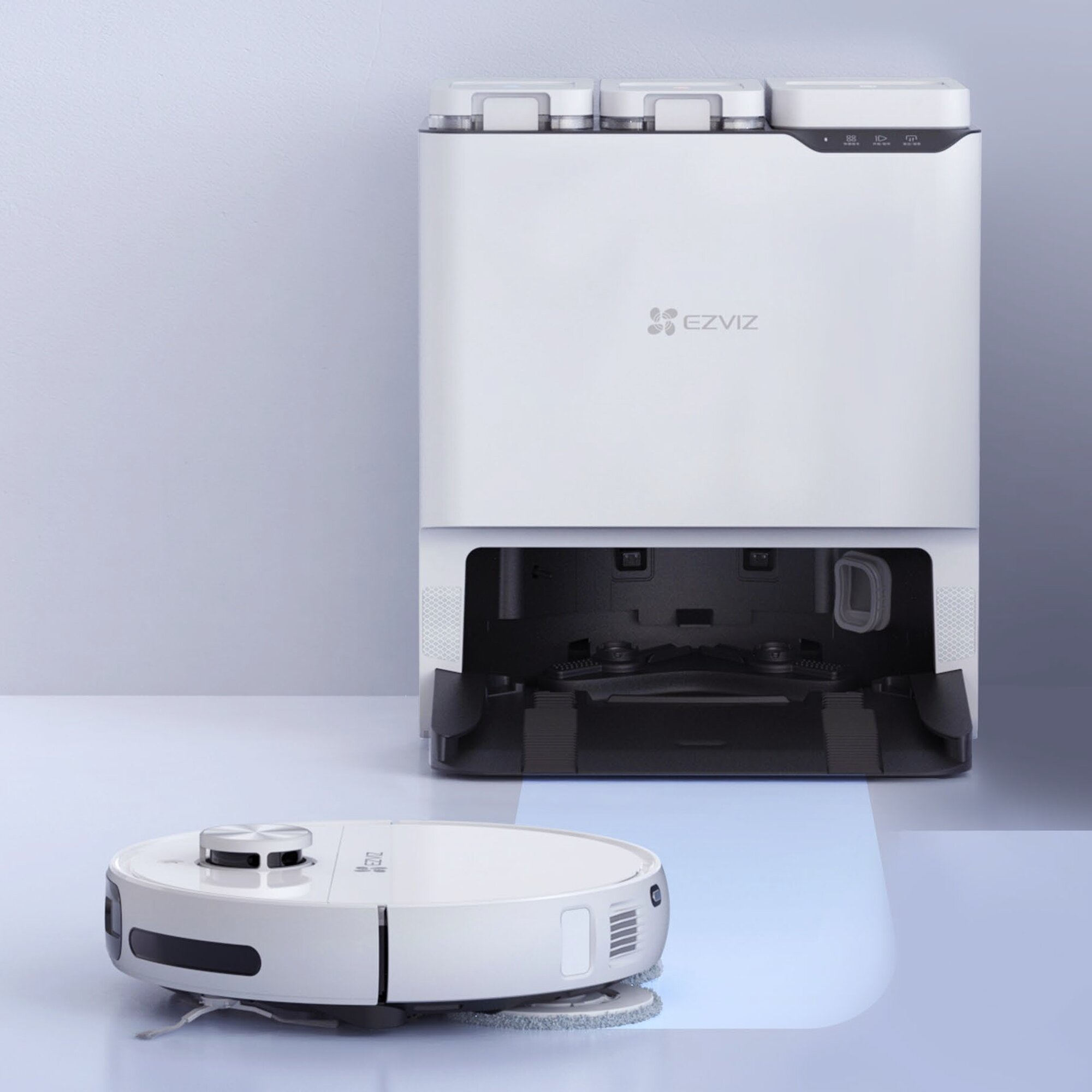 Biały odkurzacz robot EZVIZ i stacja ładująca. Odkurzacz jest na podłodze, stacja z tyłu.