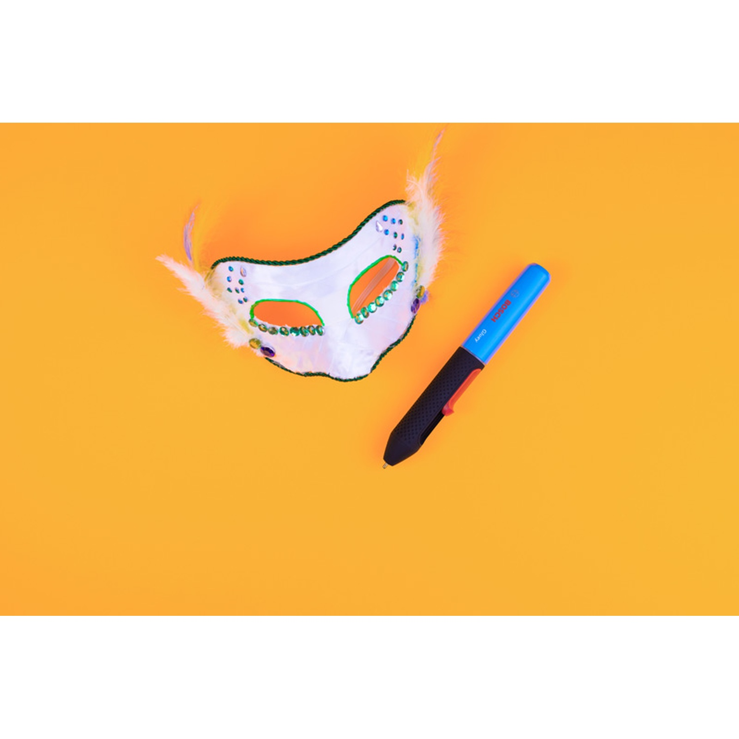 Una maschera decorativa bianca e verde con piume e una penna blu e nera su sfondo arancione.