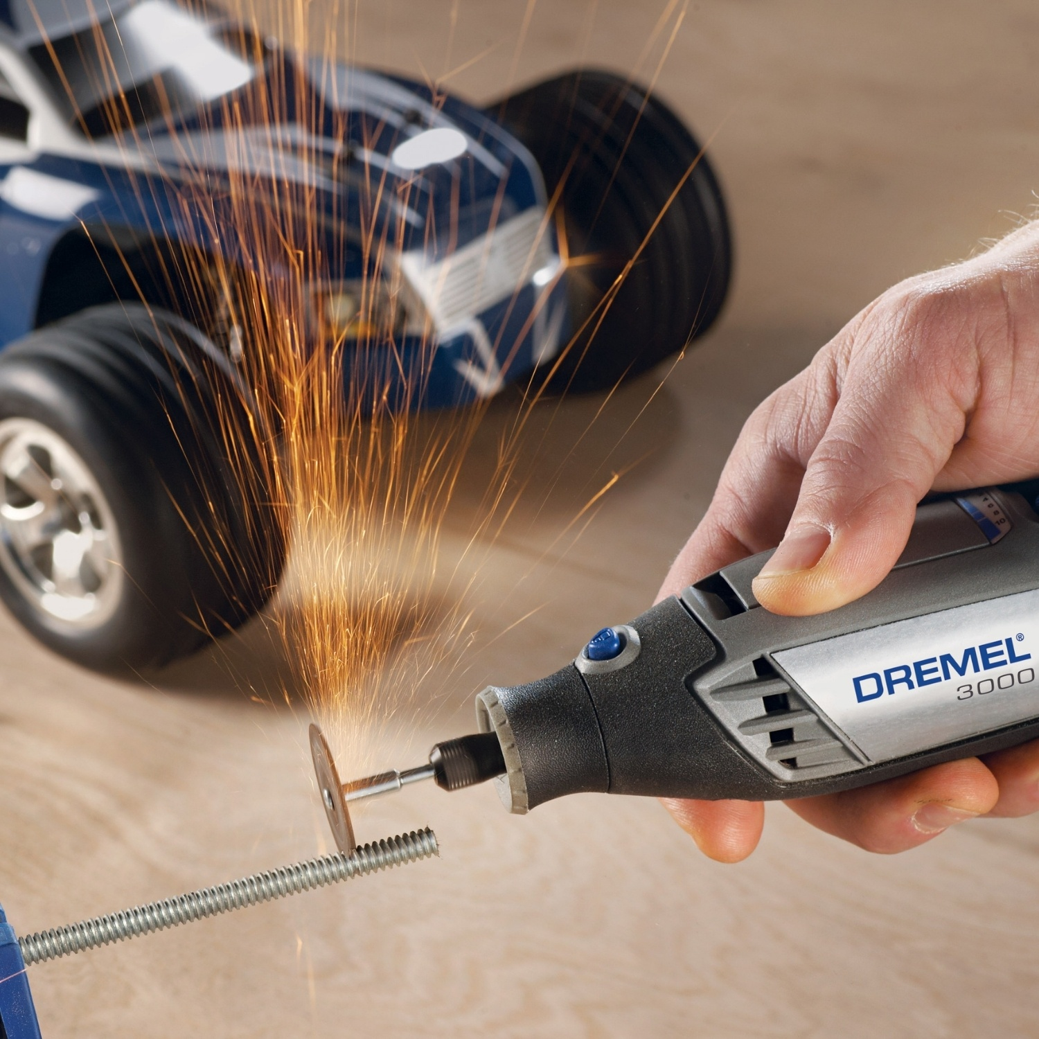 Una mano usa un Dremel per tagliare un bullone, scintille che volano. Un'auto RC blu sullo sfondo.
