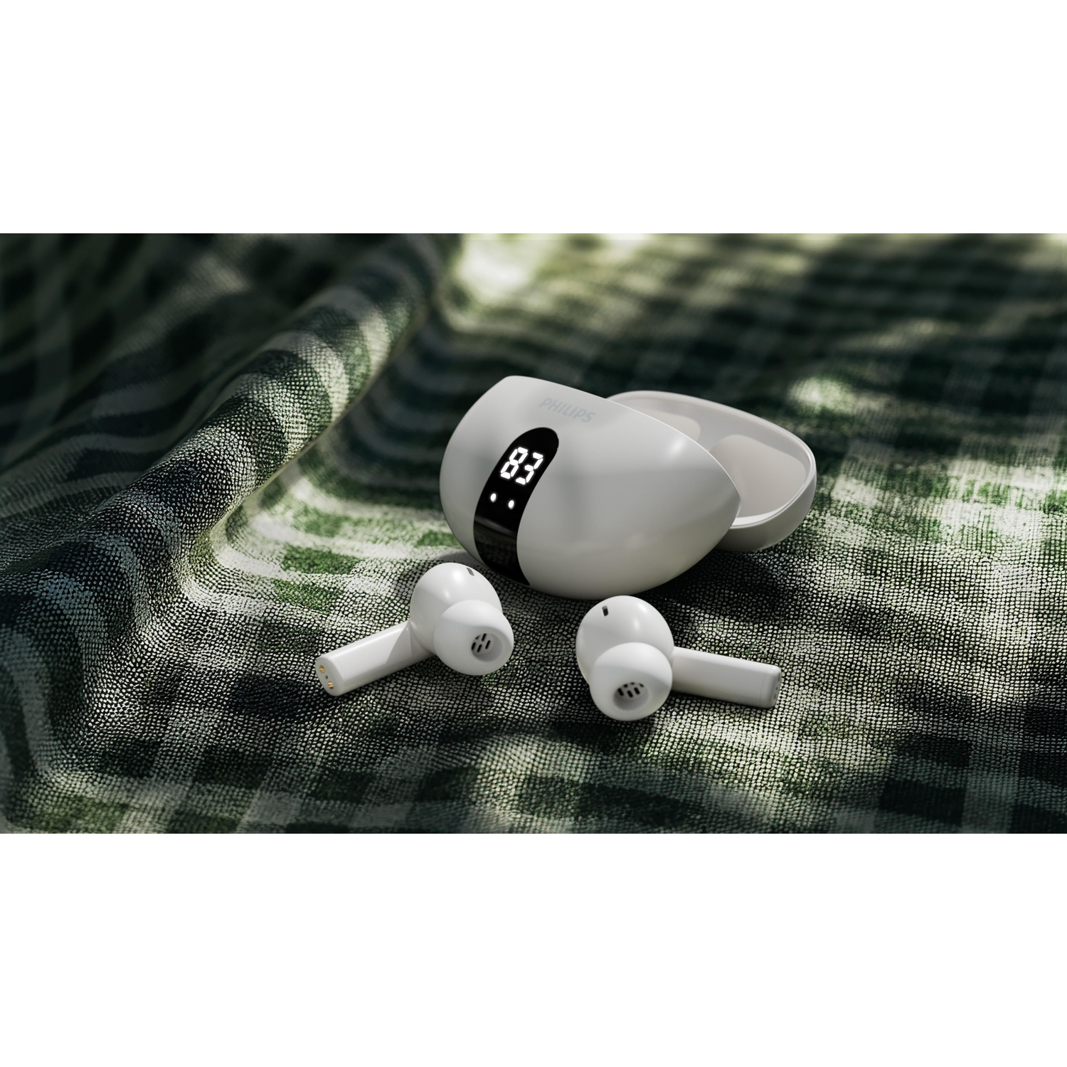 Auricolari Philips bianchi con custodia di ricarica su tessuto a quadri verde, mostra 83% di batteria. Gli auricolari sono in primo piano.