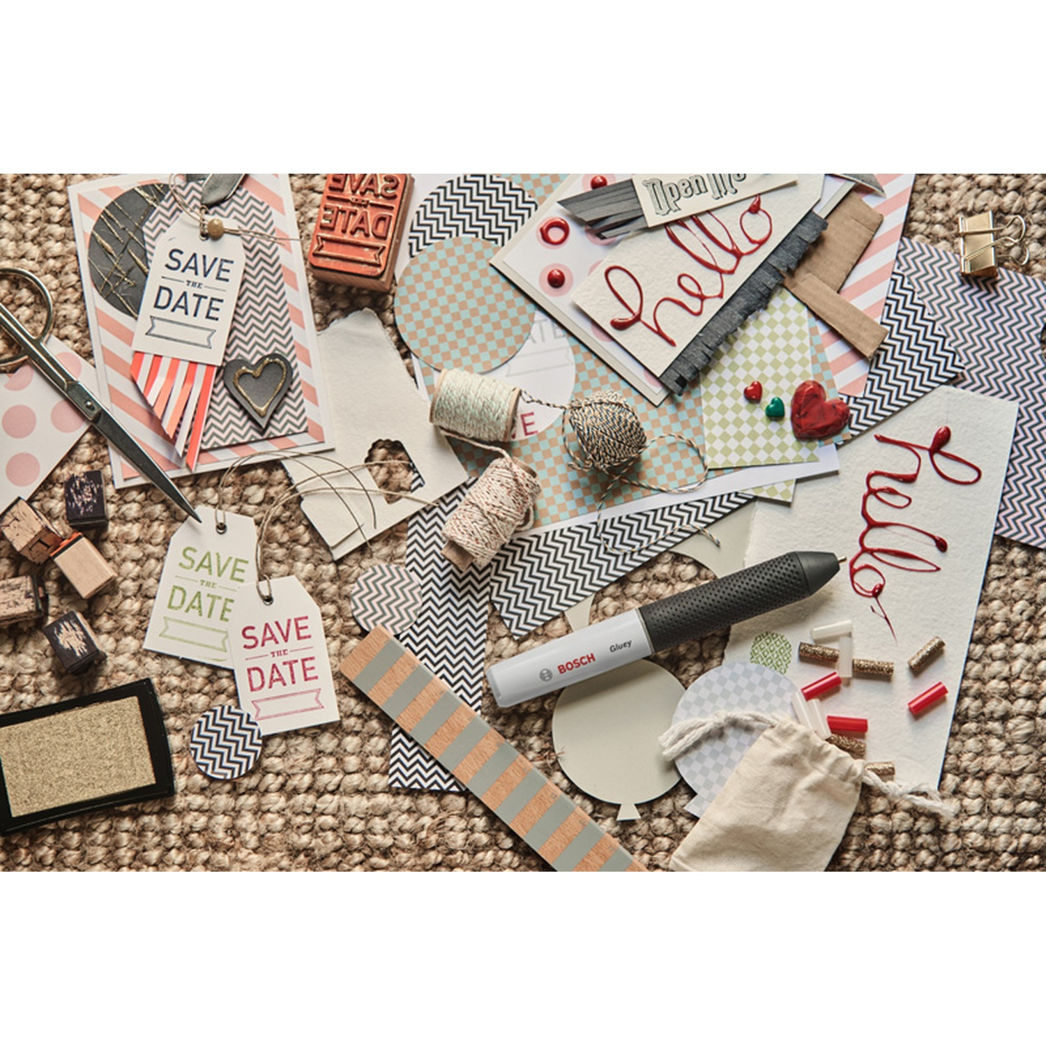 Un collage di forniture artigianali, tra cui forbici, etichette con scritto "Save the Date", una pistola per colla e "ciao" scritto a mano in rosso.