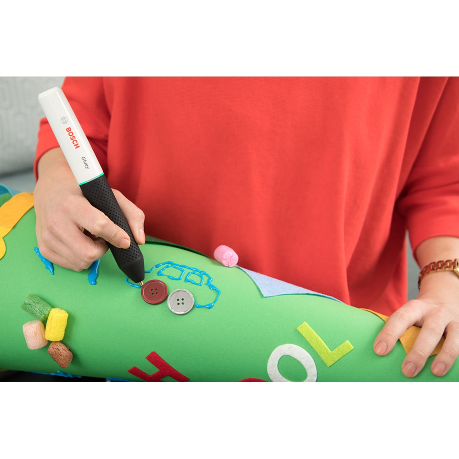 Una persona sta usando una penna colla Bosch per disegnare su un cono verde. Bottoni e lettere sono sul cono. La persona indossa una camicia rossa.