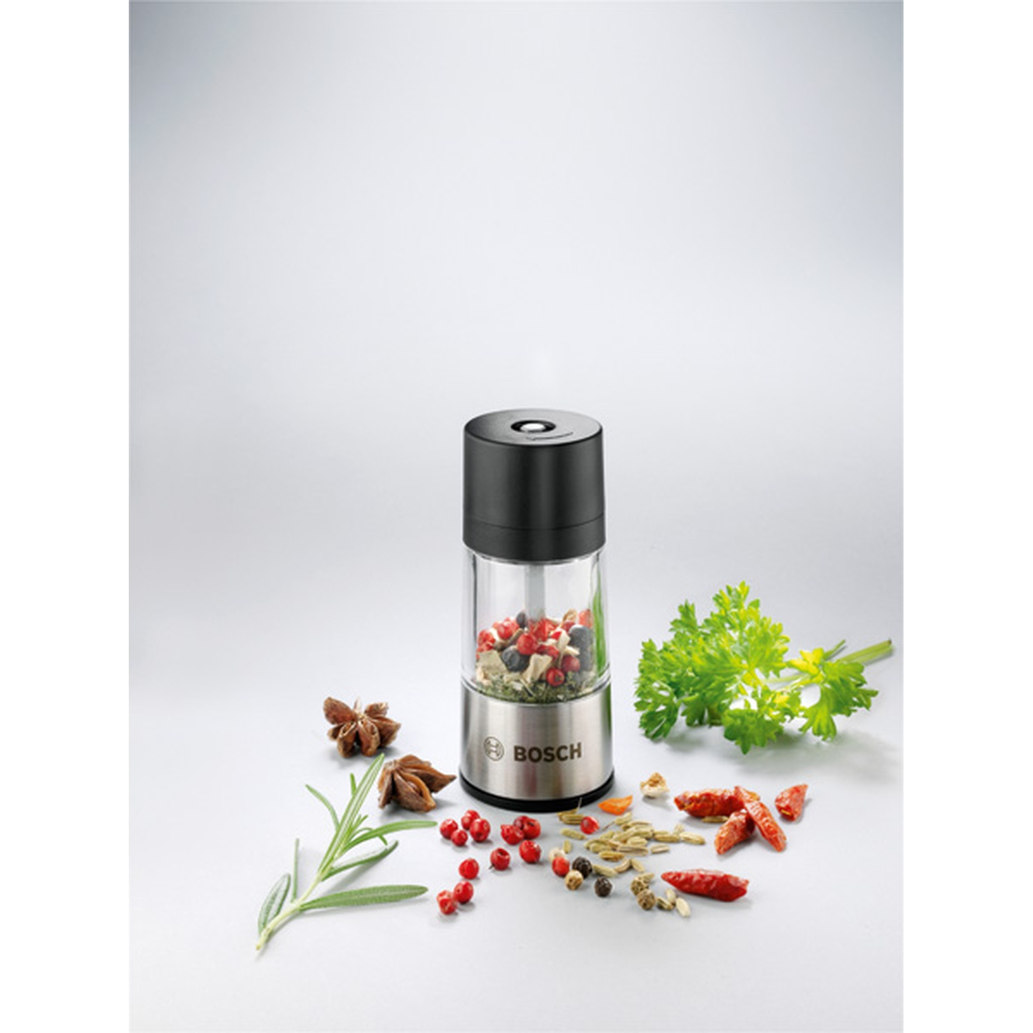 Un macinapepe con varie spezie ed erbe aromatiche. Anice stellato, rosmarino, peperoncini rossi, prezzemolo e grani di pepe sparsi.