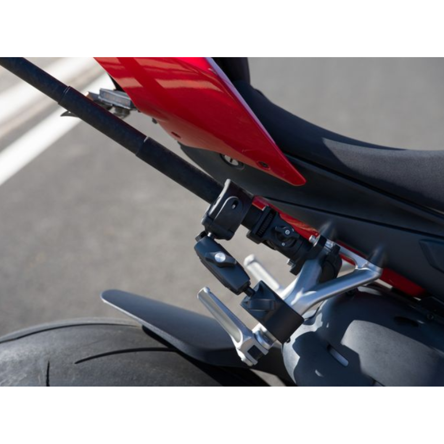Close-up of a motorcycle's rear. Red bodywork, black seat, and a detailed view of the suspension and tire. Pavement in the background.