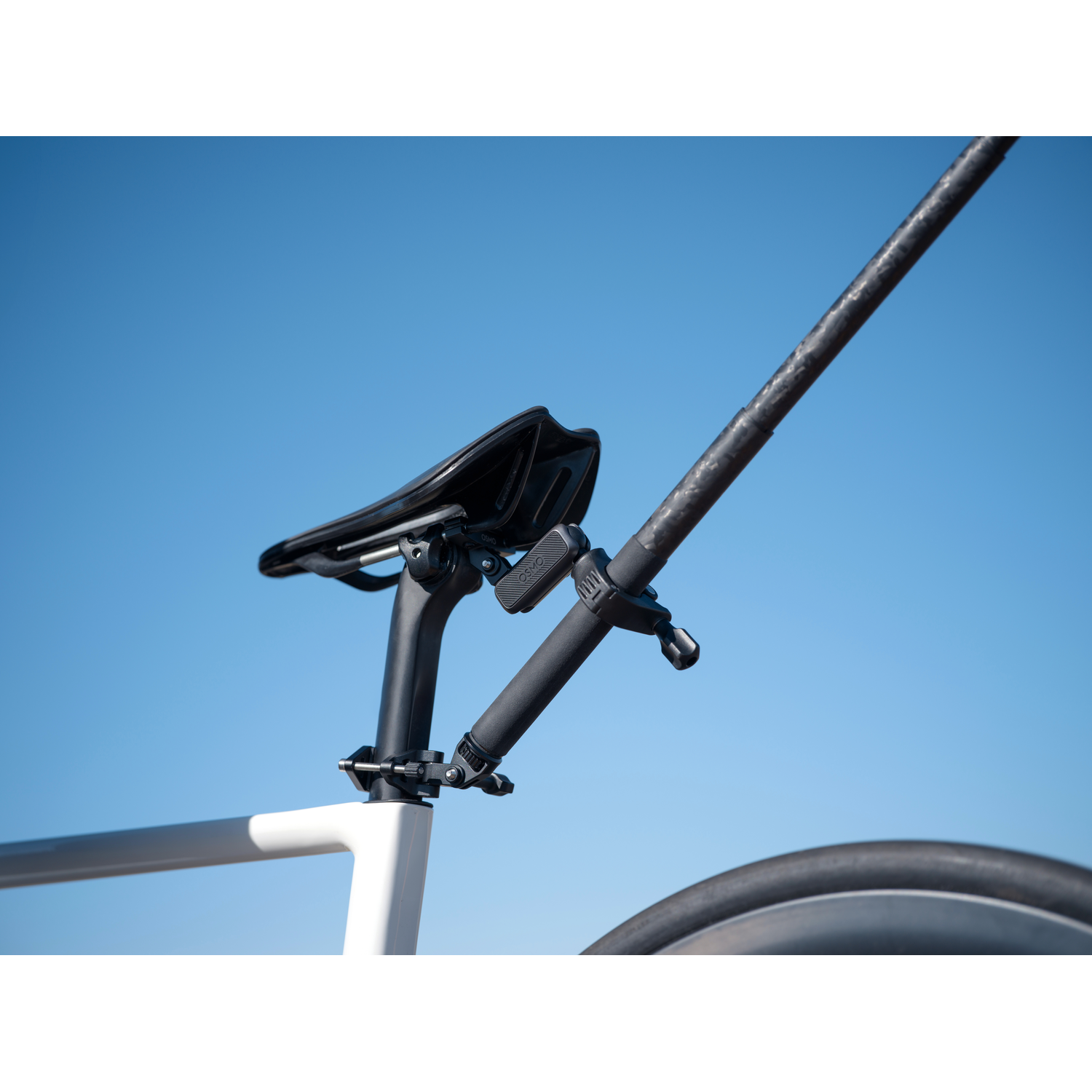 A bicycle seat and handlebars against a clear blue sky. The bike is white. The seat is black. The handlebars are black and grey.