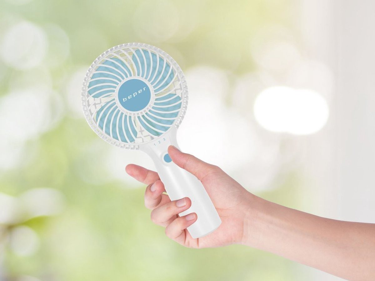 Een hand houdt een witte en blauwe draagbare ventilator vast. De ventilator heeft het merk 'beper'. Vage groene achtergrond.