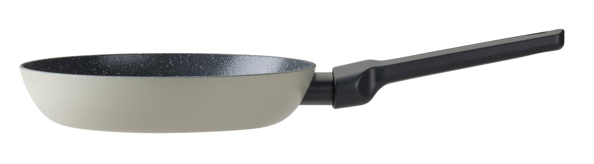 Eine hellbeige Bratpfanne mit schwarzem Griff. Das Innere der Pfanne ist mit schwarzen Punkten besprenkelt. Weißer Hintergrund.