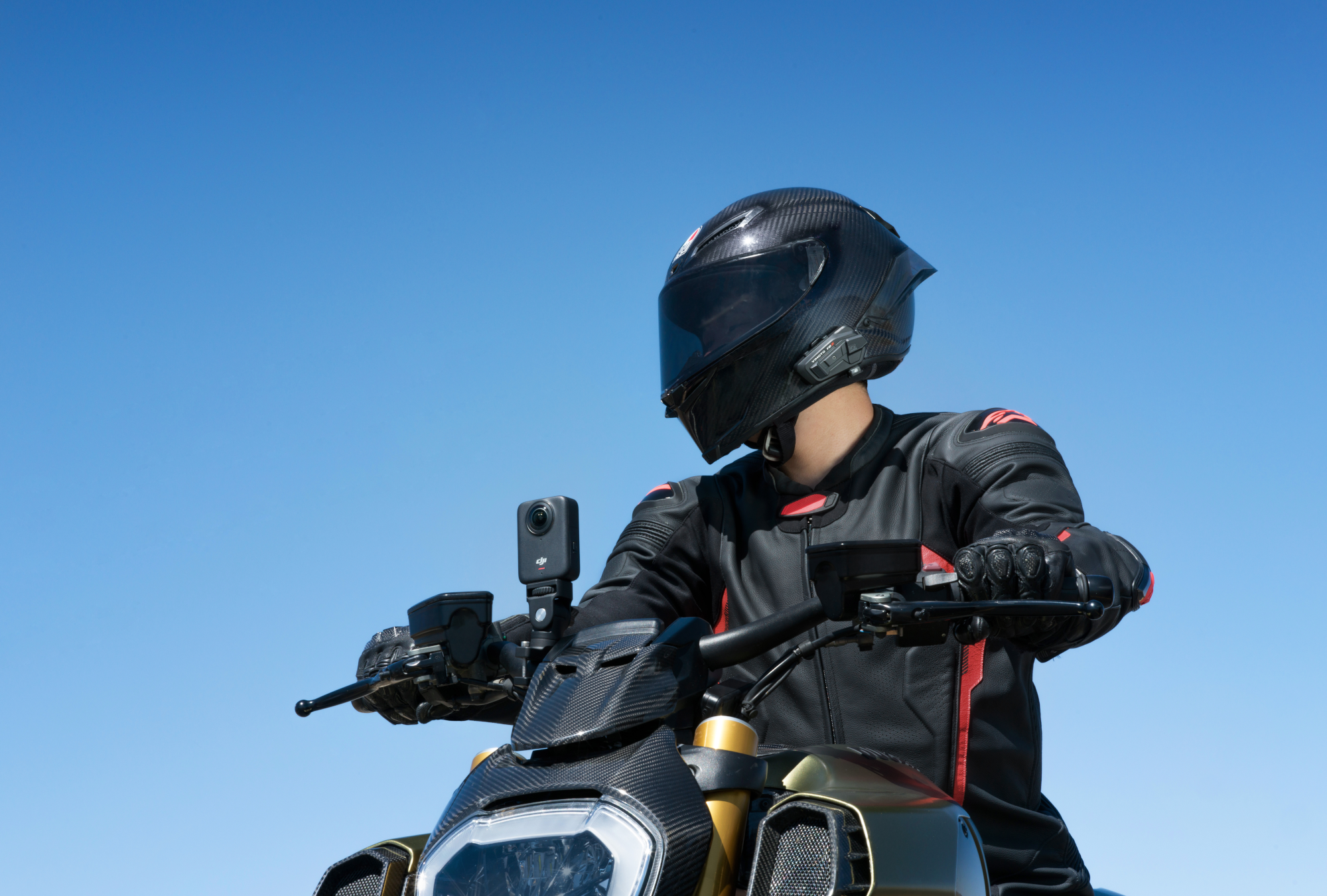 Eine Person mit schwarzem Helm und Motorradkleidung auf einem Motorrad. Klarer blauer Himmel im Hintergrund. Eine Action-Kamera ist montiert.