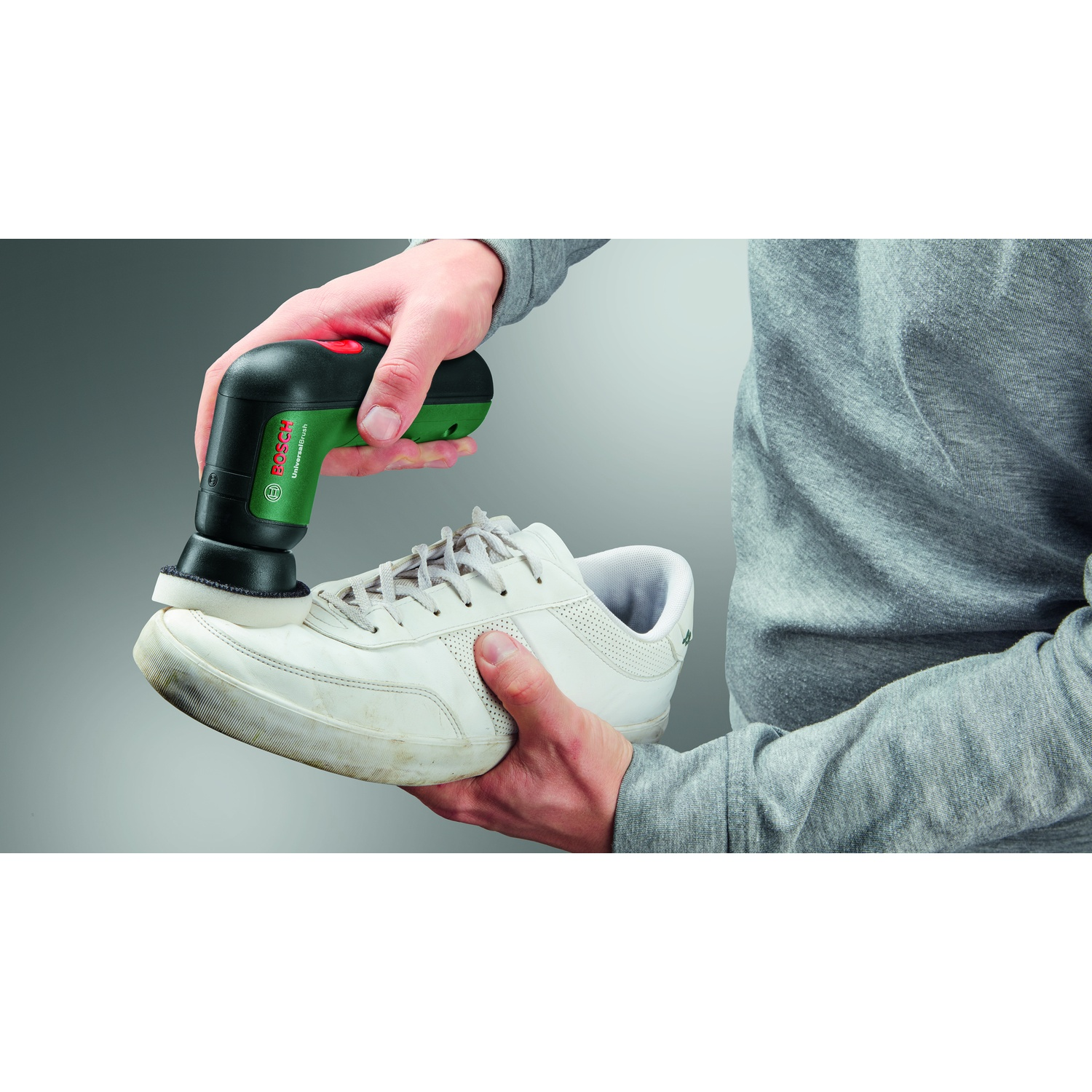 Una persona lucida una sneaker bianca sporca con una Bosch UniversalBrush nera e verde. Tengono la scarpa e la spazzola.