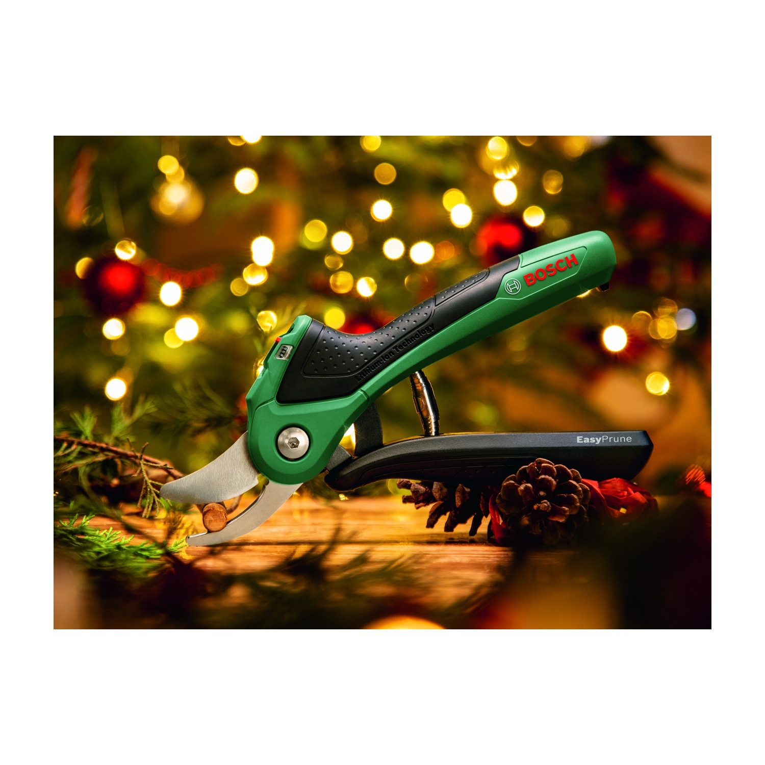 Forbici da potatura verdi Bosch EasyPrune che tagliano una noce, appoggiate su una superficie di legno. Lo sfondo è un albero di Natale sfocato con luci.