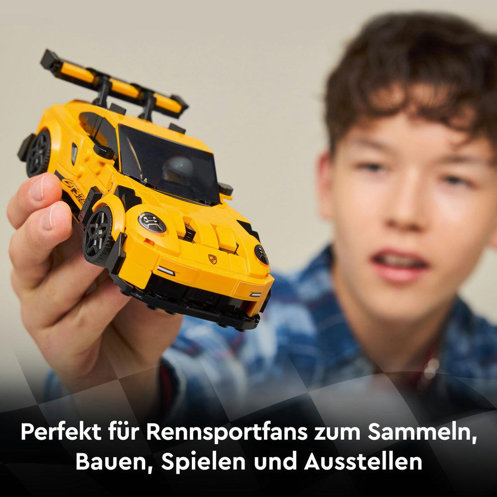 Ein gelbes Spielzeug-Rennauto wird von einer Person gehalten. Das Auto hat schwarze Details und einen Spoiler. Die Person lächelt.