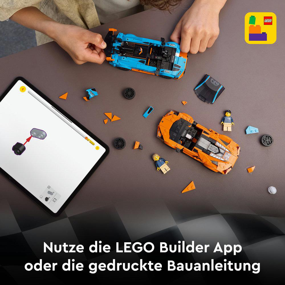 Hände, die LEGO-Automodelle zusammenbauen. Orangefarbene und blaue Autos, Minifiguren und Tablet mit Anweisungen auf brauner Oberfläche.