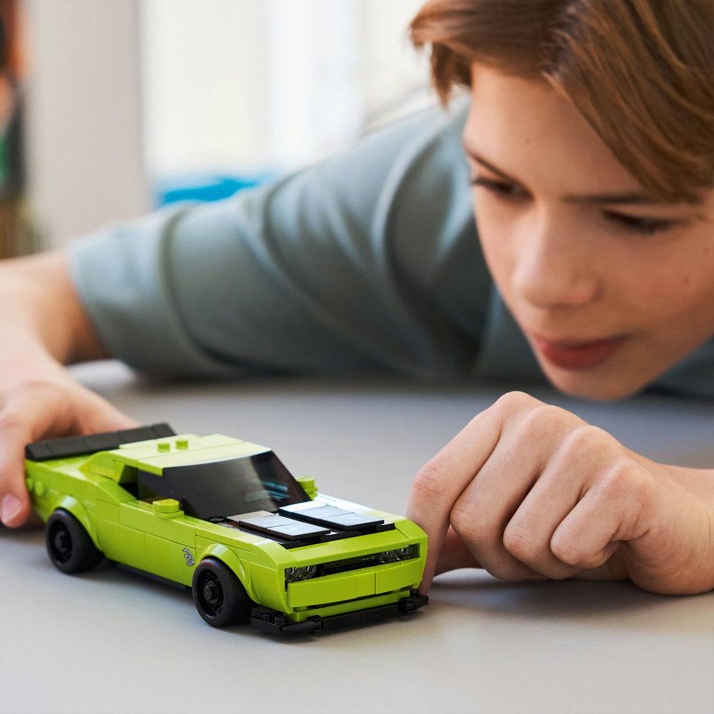 Ein Junge betrachtet ein lindgrünes Spielzeugauto. Das Auto hat schwarze Räder und ein schwarzes Dach. Der Junge trägt ein türkisfarbenes Hemd.