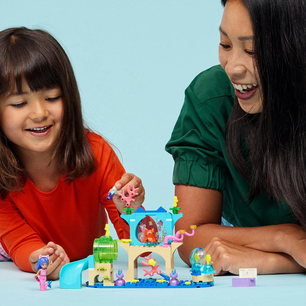 Ein Kind und eine Frau spielen mit einem Lego-Set. Das Set zeigt eine Unterwasserszene mit Figuren und Korallenriffen.