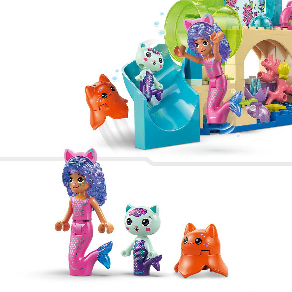 Ein Spielzeugset mit Meerjungfrauenfiguren mit Katzenohren. Es gibt eine blaue Rutsche und eine orangefarbene Katzenfigur. Der Hintergrund ist weiß.