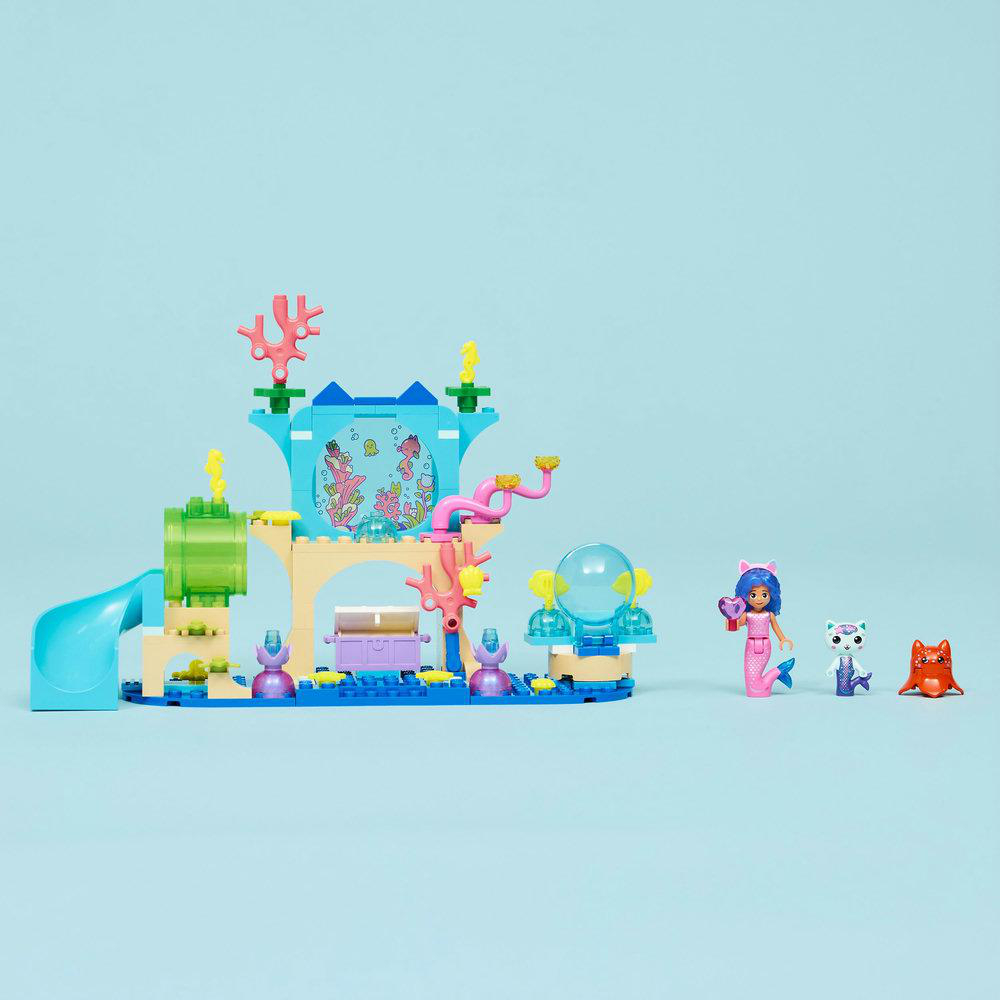 Eine Lego-Unterwasserszene mit Gebäuden, einer Rutsche und Figuren, darunter eine Meerjungfrau und Tierfiguren, auf blauem Hintergrund.