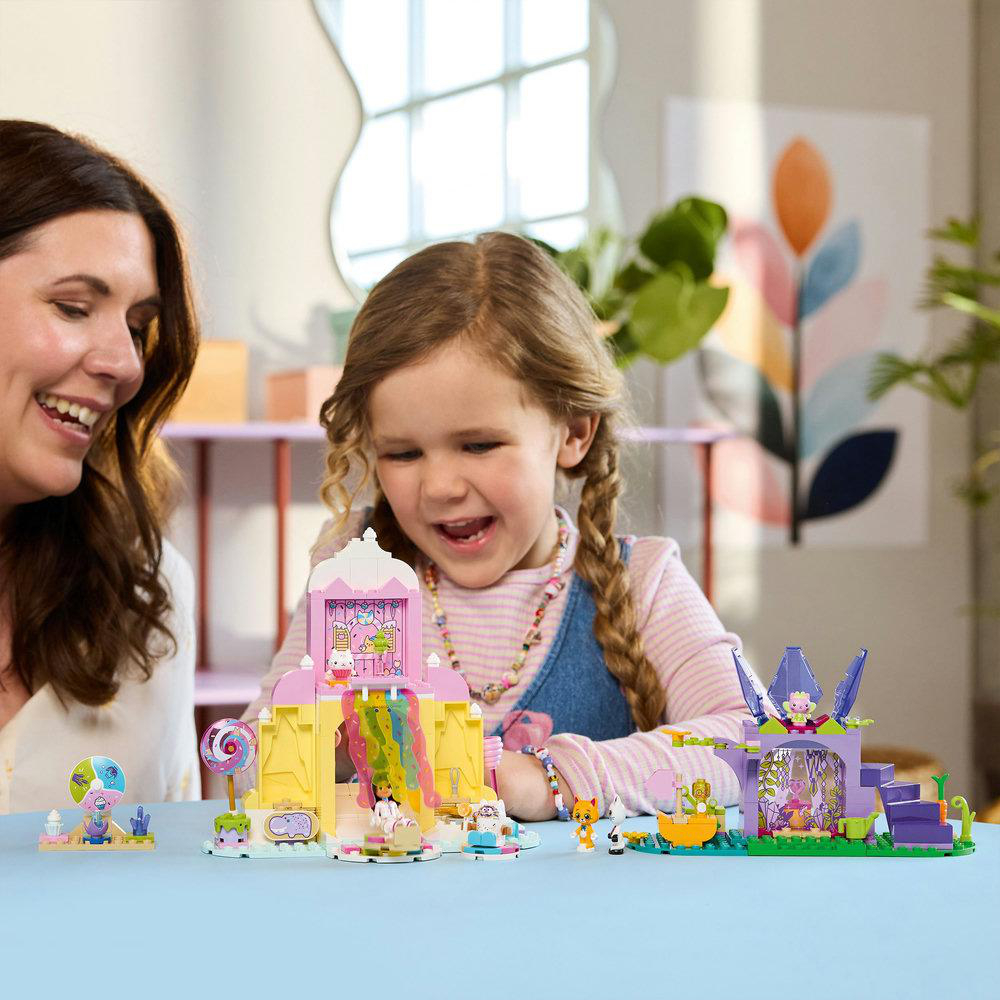 Eine Frau und ein Mädchen lächeln ein Spielzeug an. Das Set enthält eine Rutsche, ein Gebäude und andere kleine Spielfiguren.