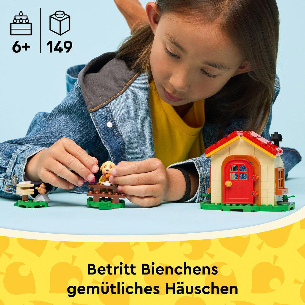 Ein Mädchen spielt mit einem Lego-Set. Das Set enthält ein kleines Haus mit roter Tür und Dach sowie Lego-Figuren und Bäume.