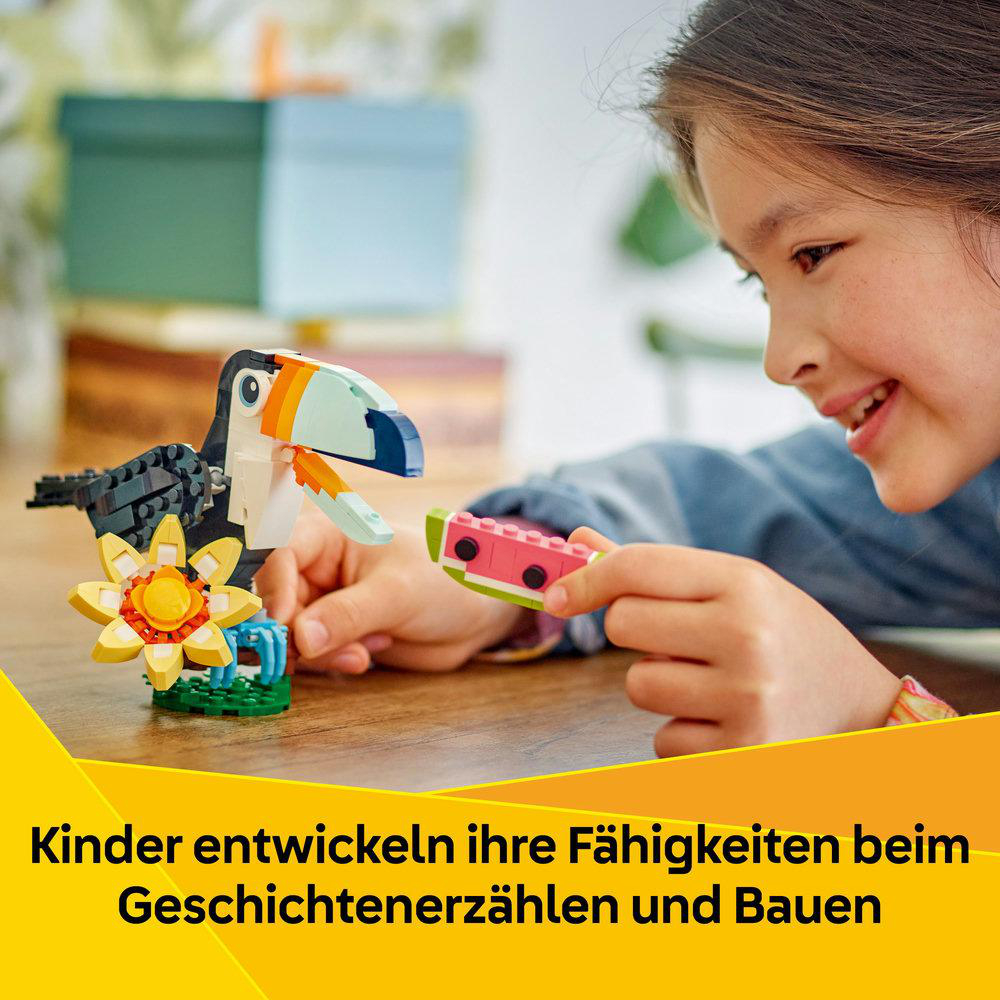 Ein Mädchen lächelt, während es einen Lego-Tukan und eine Wassermelone baut. Auf dem Tisch liegt eine gelbe Blume. Text: Kinder entwickeln Fähigkeiten.