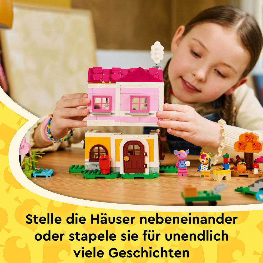 Ein Mädchen hält Spielzeughäuser. Die Häuser sind rosa und gelb. Andere Spielzeuge liegen auf dem Tisch.