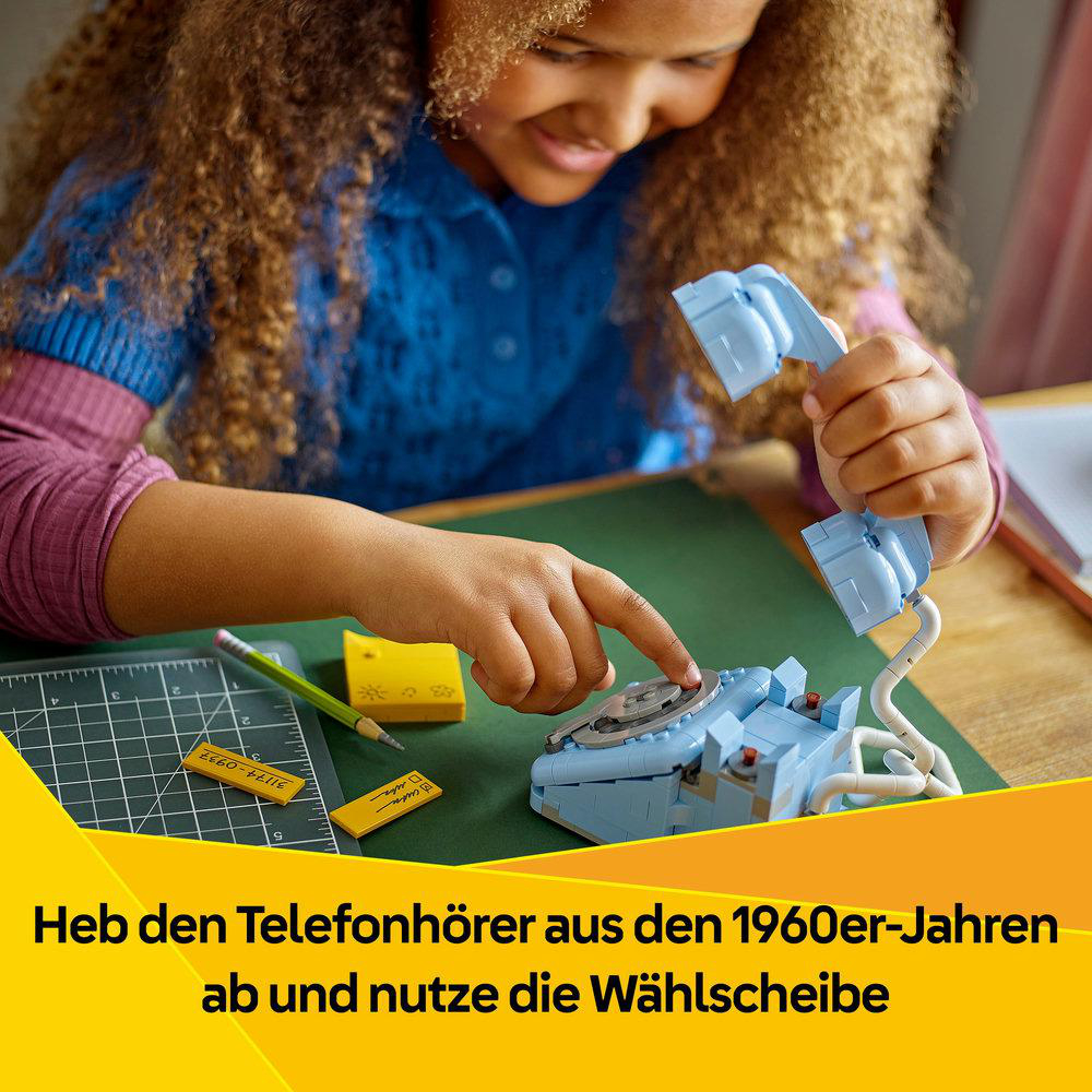 Ein Mädchen spielt mit einem hellblauen LEGO-Telefon aus den 1960er Jahren. Sie hält den Hörer und berührt die Wählscheibe.
