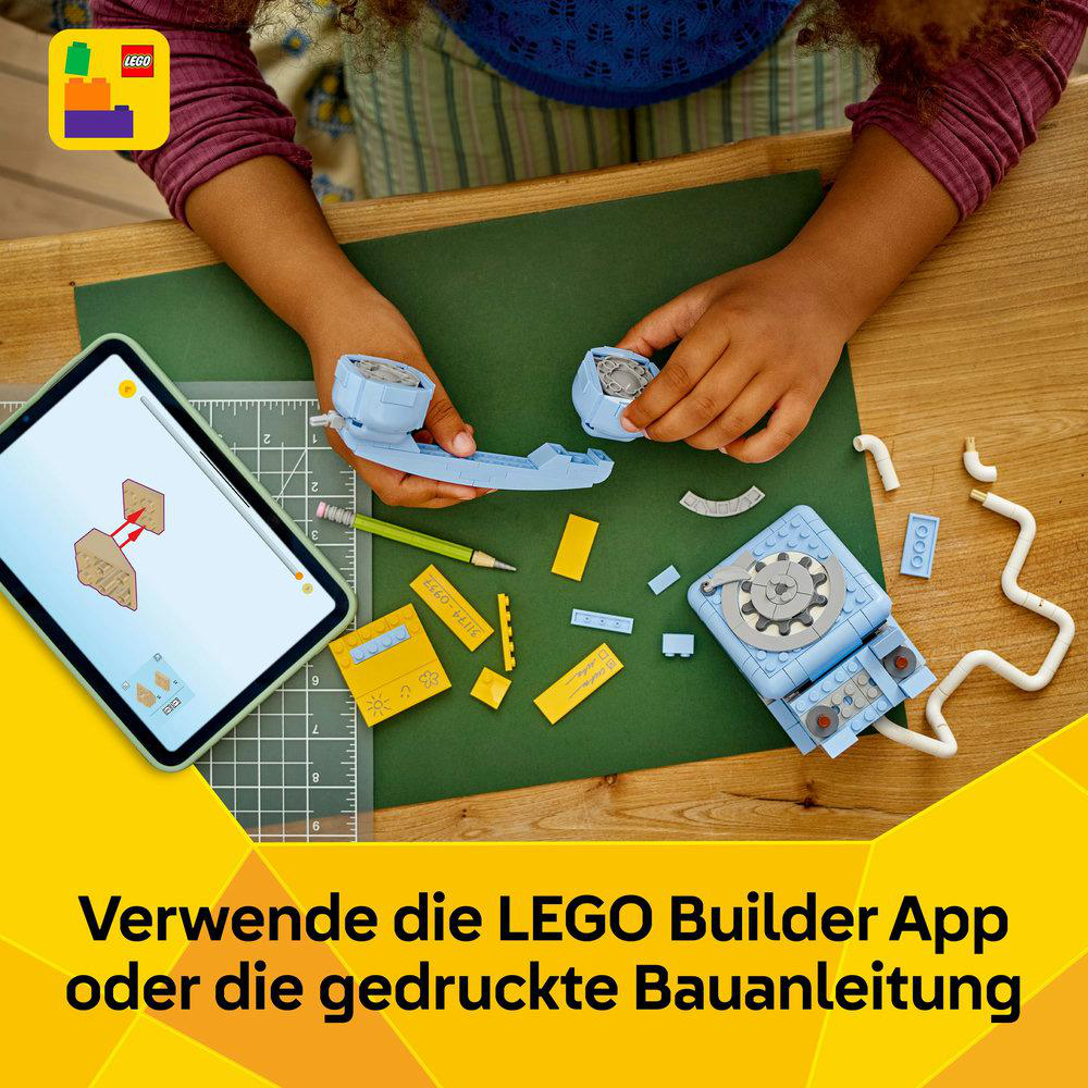 Ein Kind, das Lego-Teile zusammenbaut und sich dabei auf Anweisungen auf einem Tablet bezieht. Verschiedene Lego-Teile und eine grüne Schneidematte sind sichtbar.