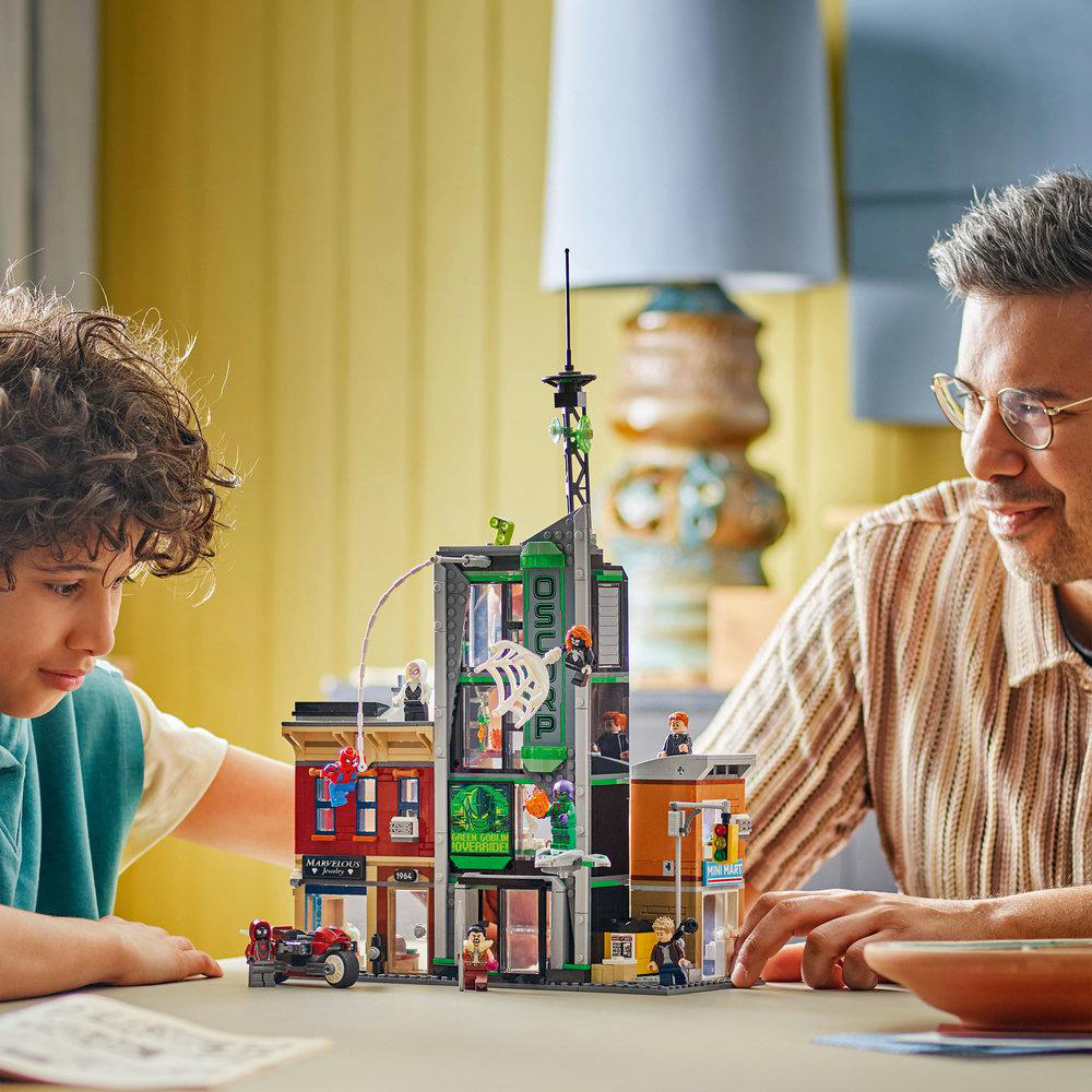 Ein Vater und sein Sohn betrachten ein Lego-Set eines Gebäudes. Das Set enthält Spider-Man und andere Miniaturfiguren und ein Motorrad.