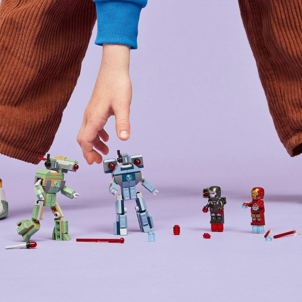 Hand über Lego-Robotern. Grüne, blaue und rote Roboter auf einer lila Oberfläche. Braune Hose und blaue Hemdsärmel sind sichtbar.