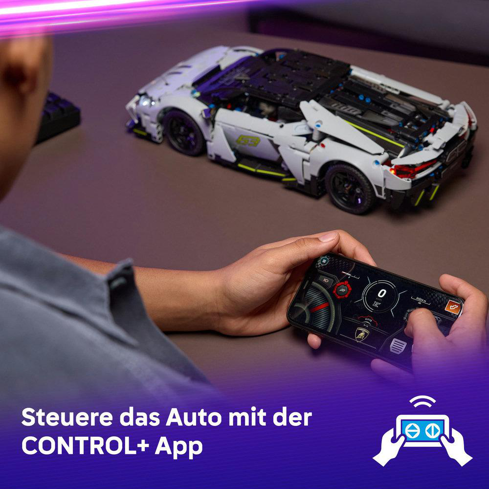 Eine Person hält ein Telefon, das ein weißes und schwarzes Spielzeugauto steuert. Das Auto steht auf einer braunen Oberfläche. Das Telefon zeigt eine Autoschnittstelle.