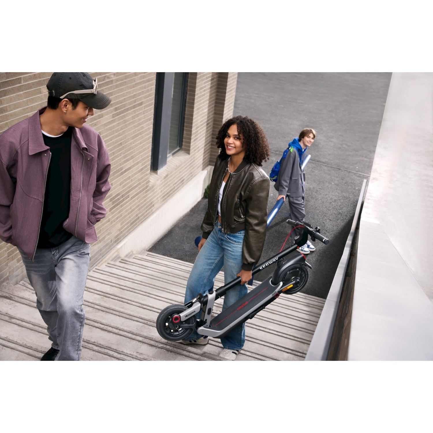 Una donna porta uno scooter, scendendo le scale con due persone. Un uomo scende e un altro sale le scale.