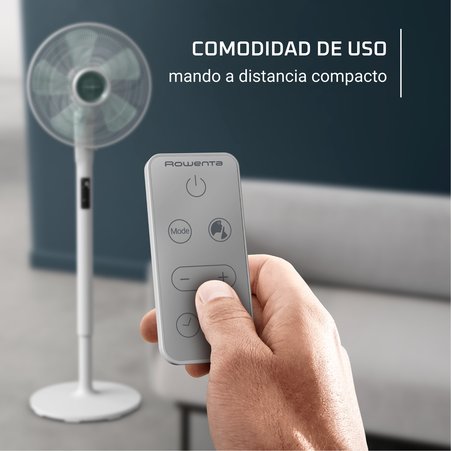 A hand holding a remote control for a white fan. The fan is in the background. Text reads 'COMODIDAD DE USO mando a distancia compacto'.