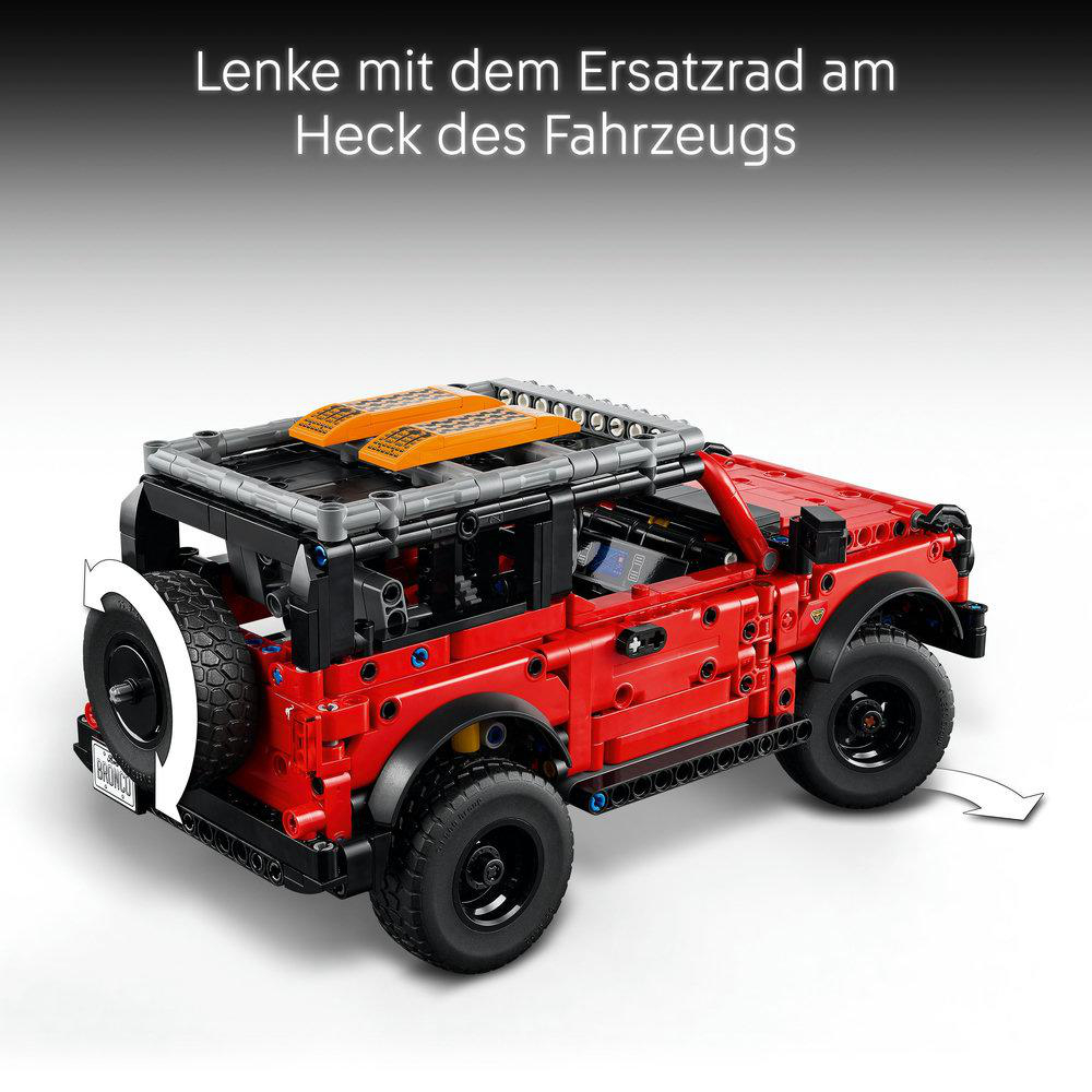 Ein rotes Spielzeugauto mit Reserverad hinten. Es hat schwarze Räder und ein schwarzes Dach mit orangefarbenen Paneelen.