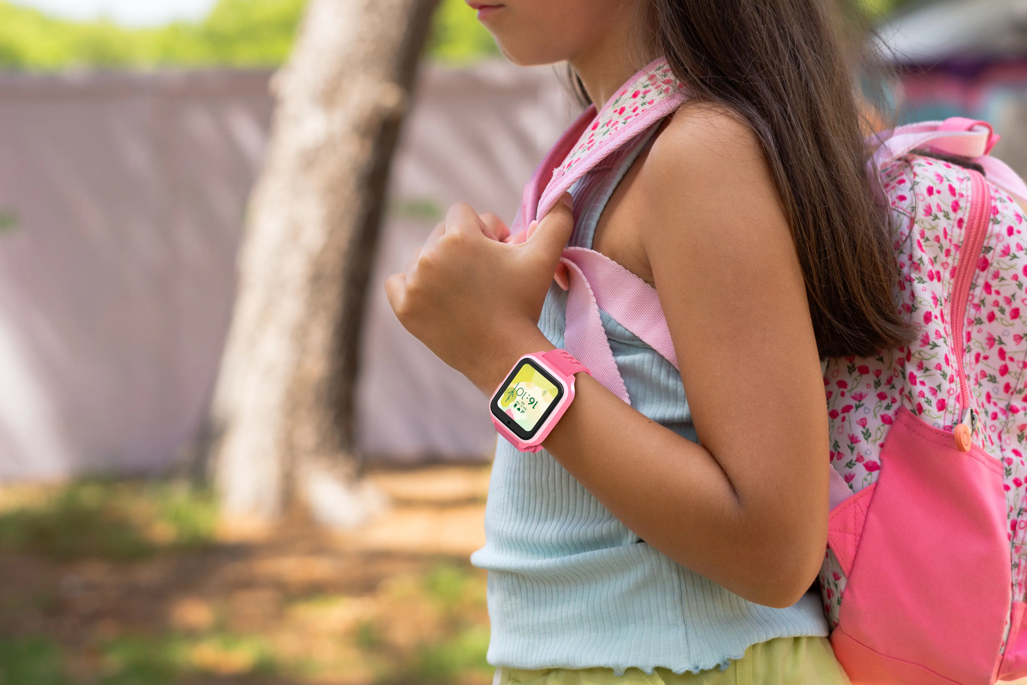 Une fille portant une montre connectée rose et un sac à dos à motifs floraux. À l'extérieur, tenant la sangle.