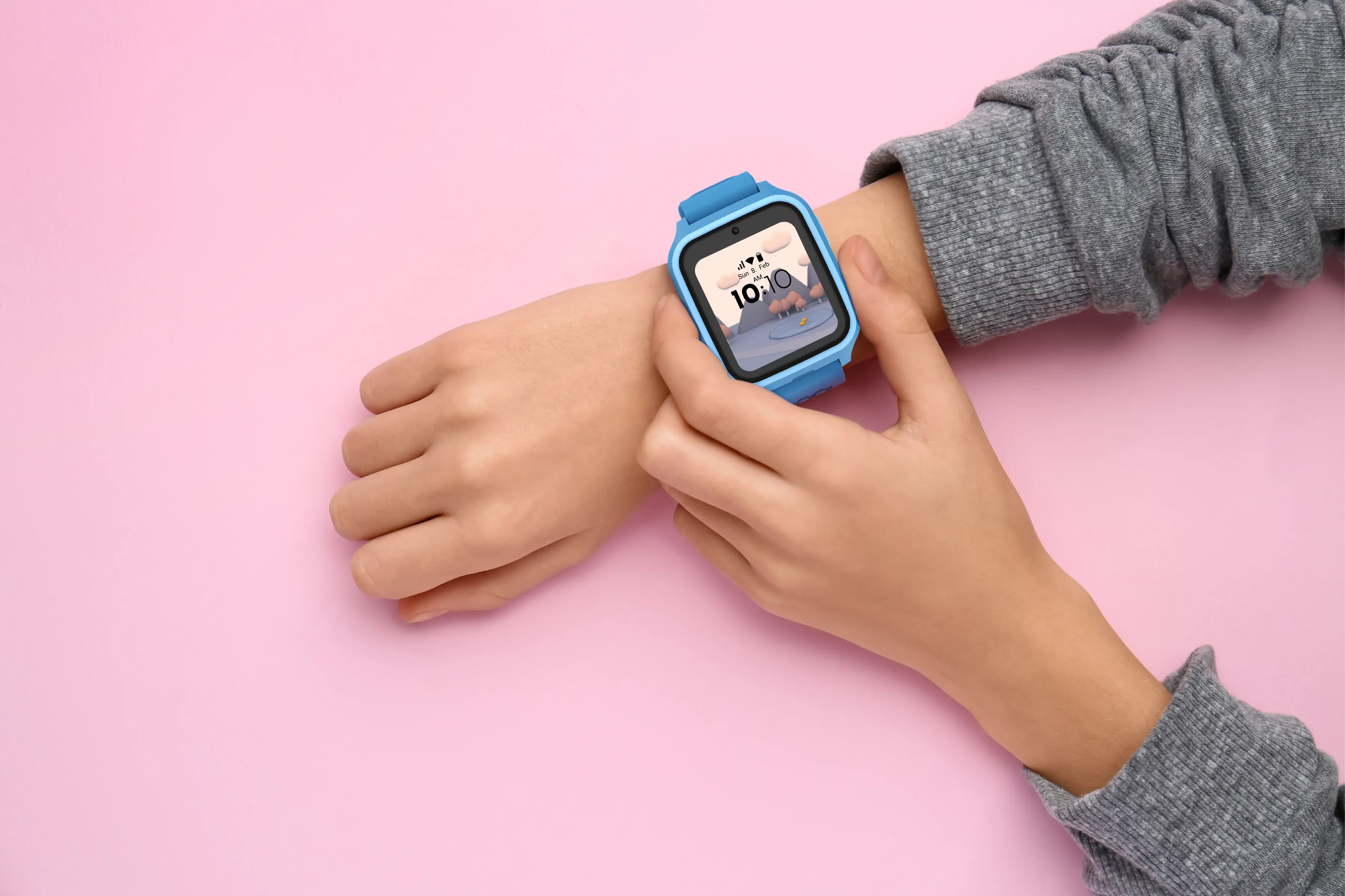 Le poignet d'une personne avec une montre intelligente bleue affichant l'heure, sur fond rose. La personne porte un pull gris.