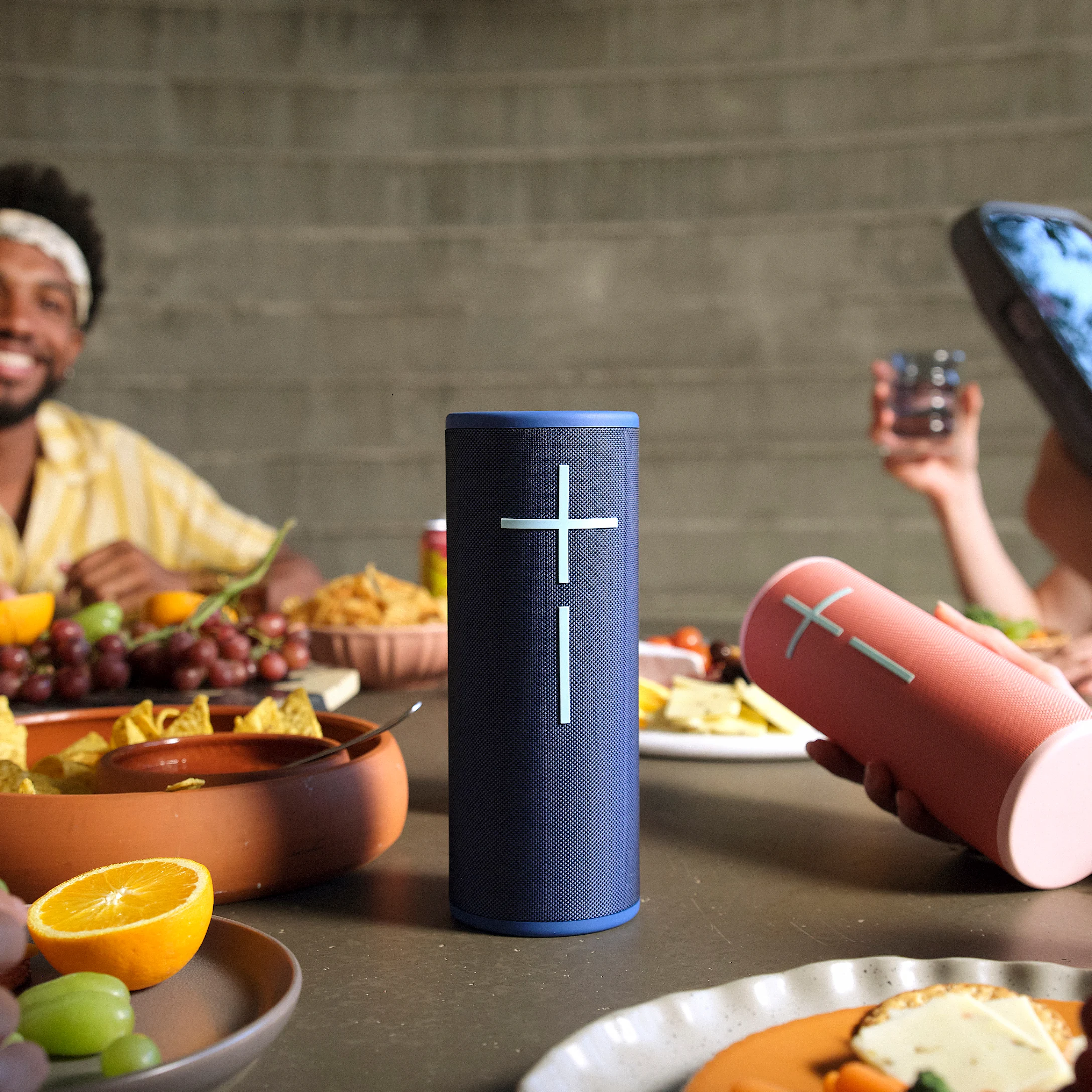 Une table avec de la nourriture et des boissons. Deux haut-parleurs sur la table. Les gens sourient.