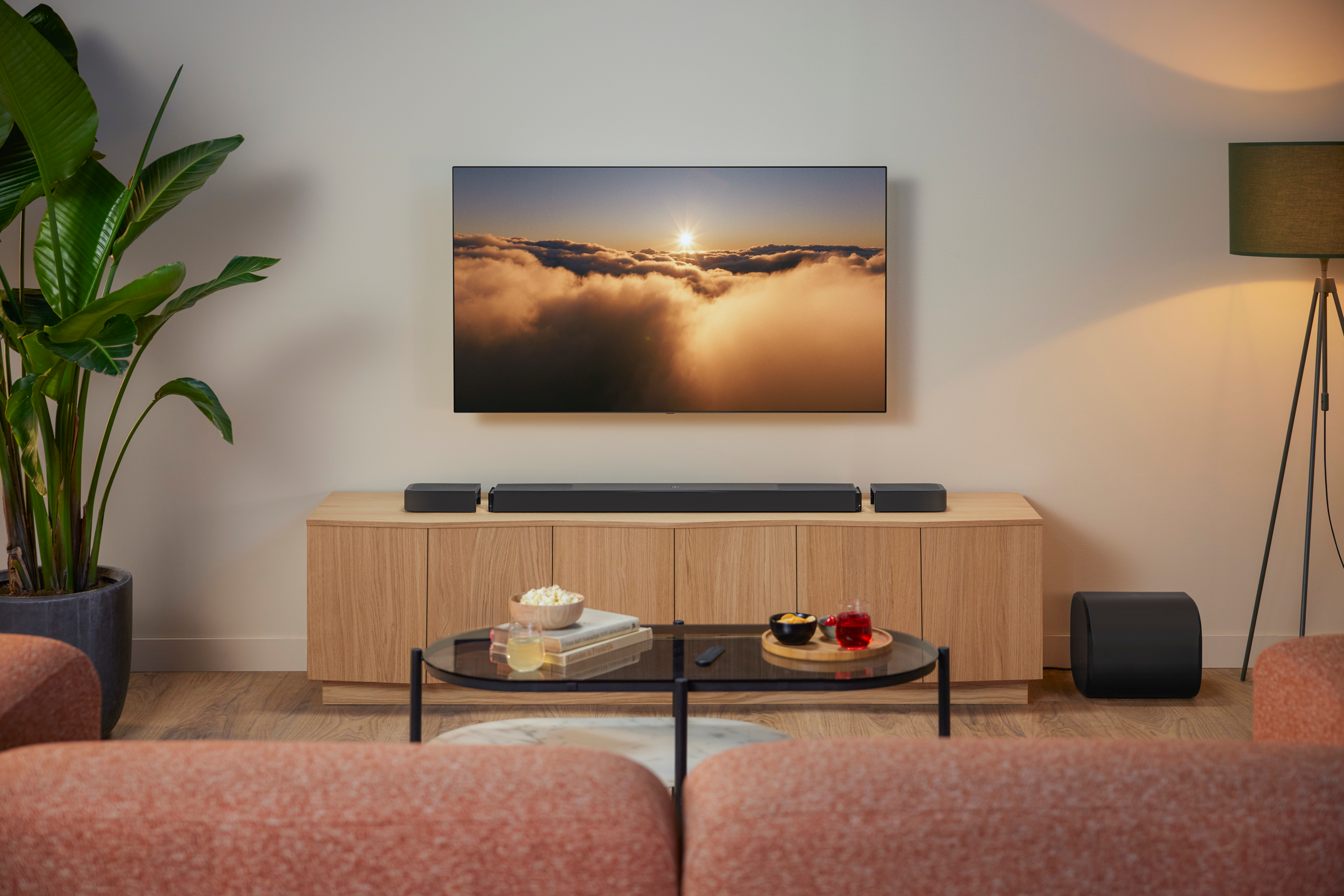 Wohnzimmer mit TV, Soundanlage, Couch, Tisch mit Snacks, Pflanze und Lampe.